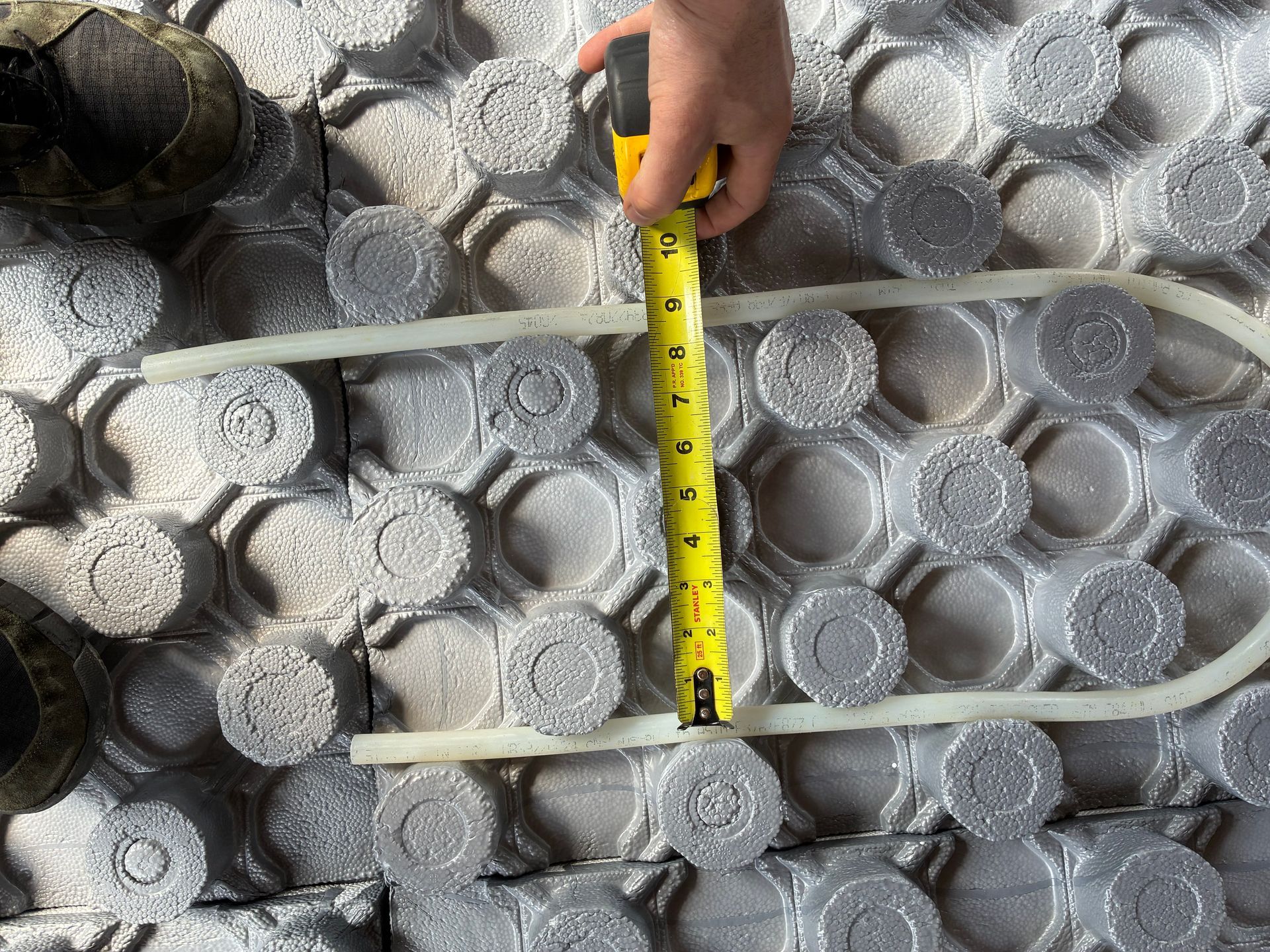 Measuring tape over gray foam tubing laid on a patterned surface, with a tool at left.