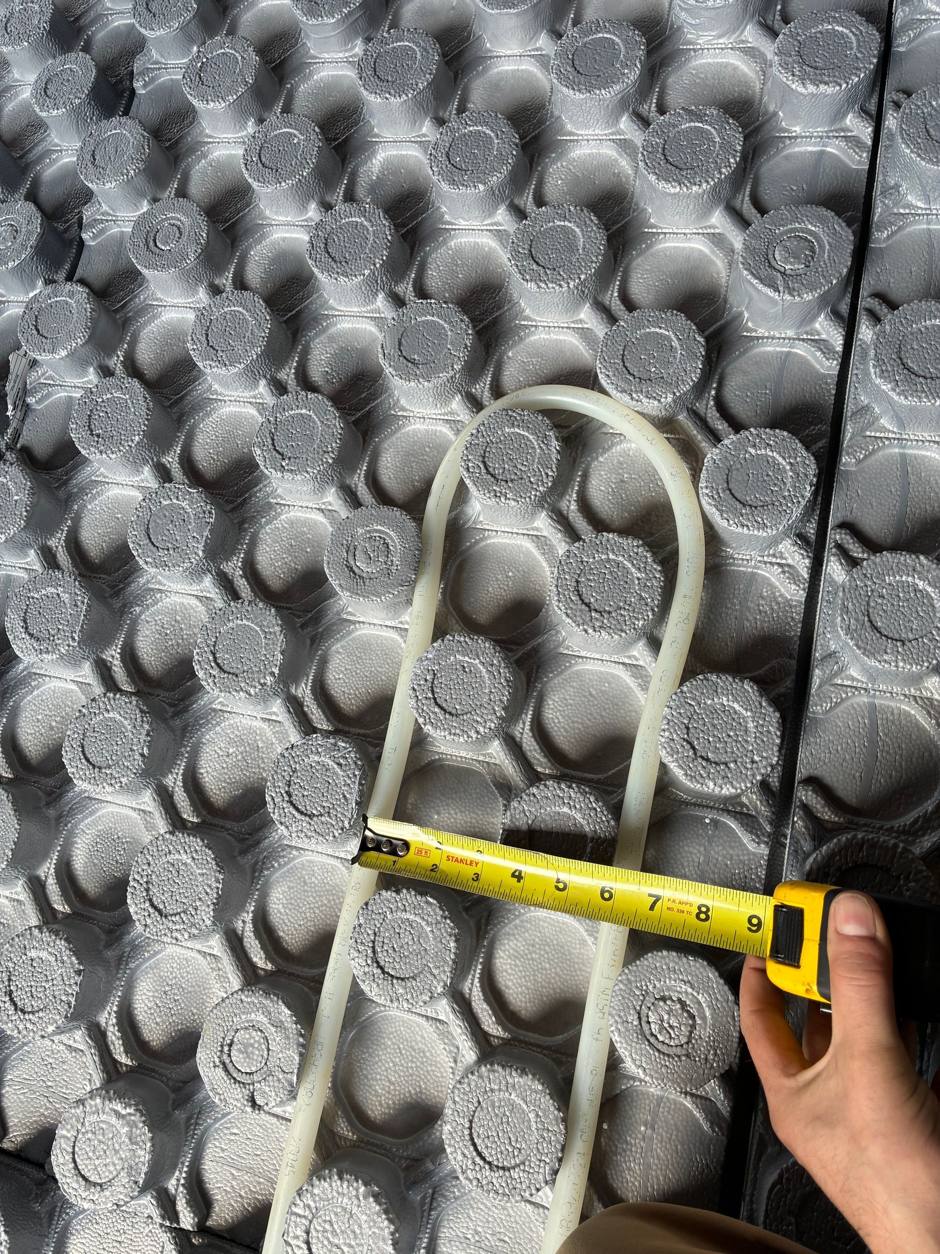 Hand holding a tape measure beside a coiled white rope on gray bubble wrap packaging