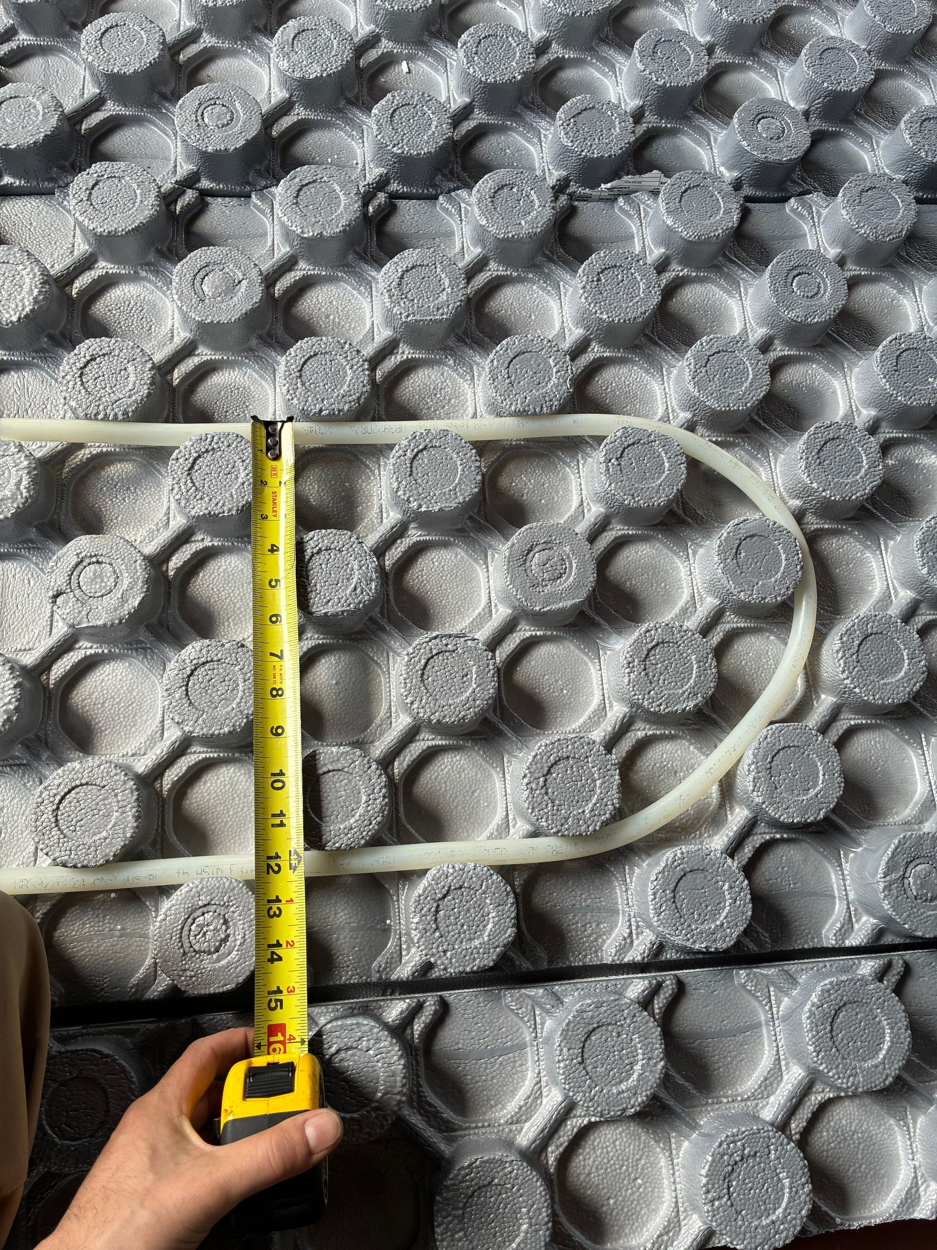 Yellow measuring tape beside a beige cable looped on a textured gray mat.