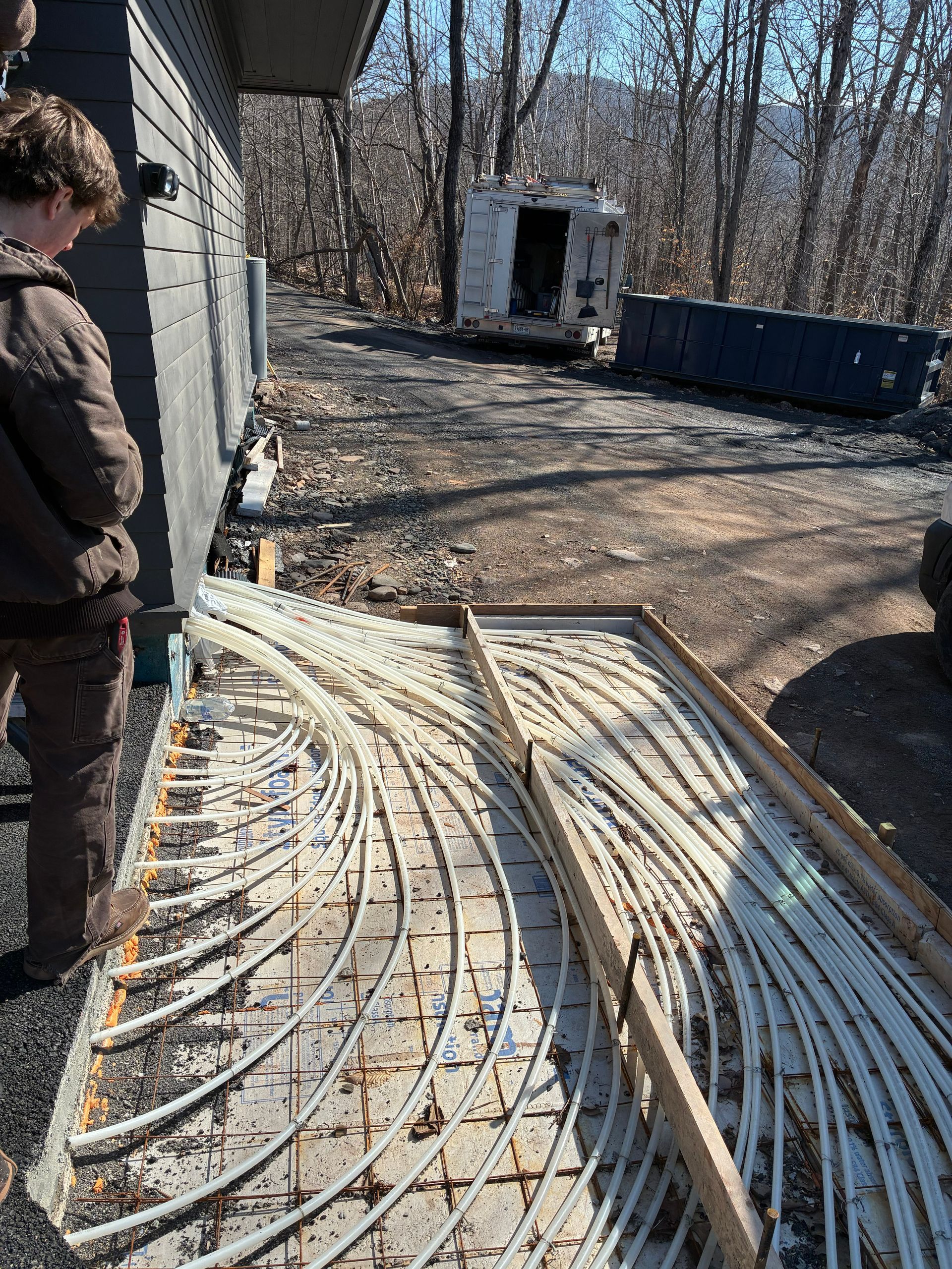Worker beside bundled cables on a gravel site next to a brick building, with a blue dumpster in the background