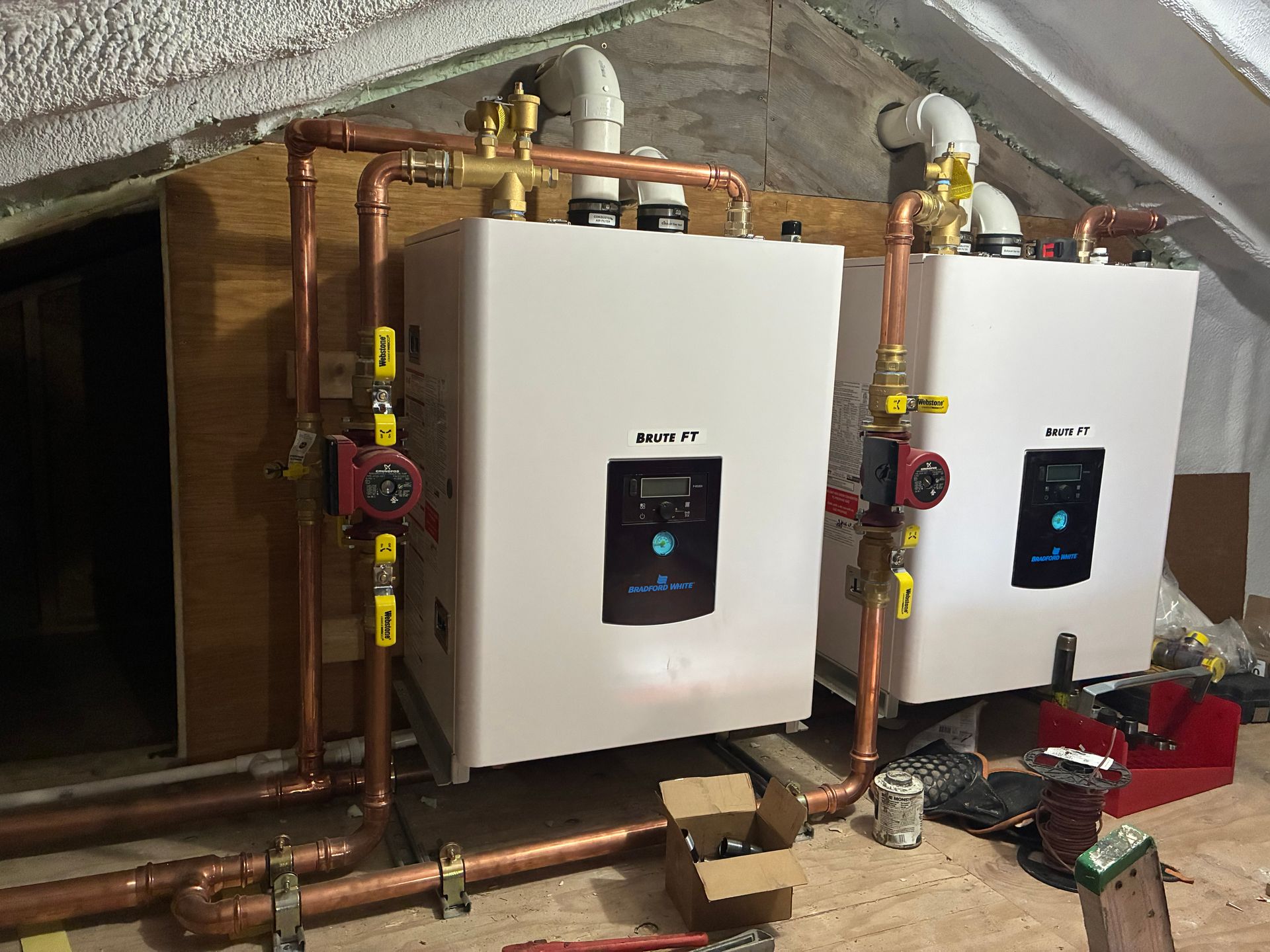 Two wall-mounted white boilers with copper pipes in a basement utility room