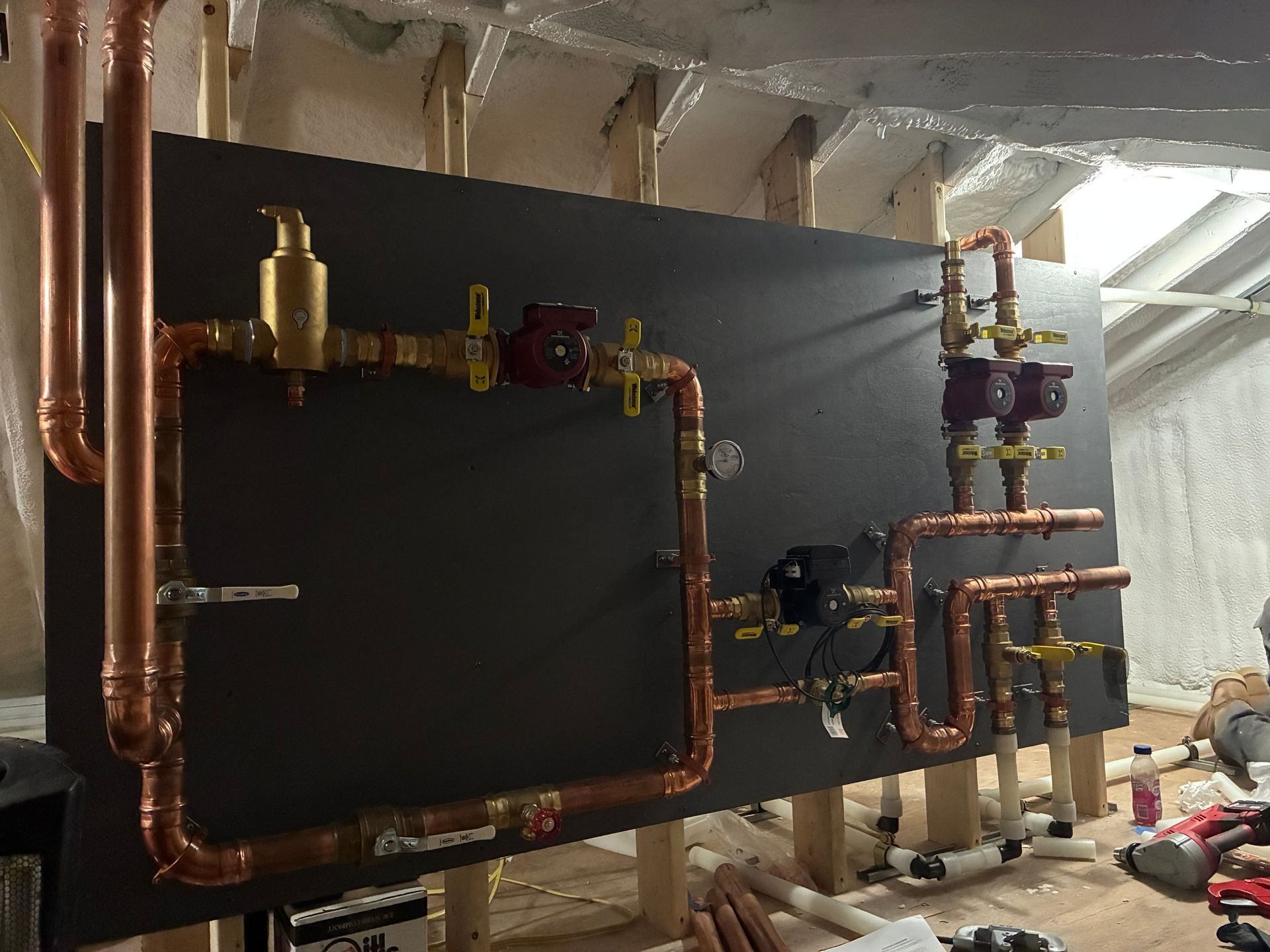 Copper pipes and valves mounted on a large black HVAC unit in a basement utility room