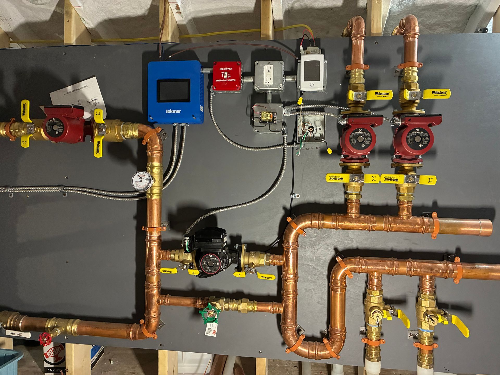 Copper pipes and valves on a wall, with red and blue control boxes and gauges in a mechanical room.