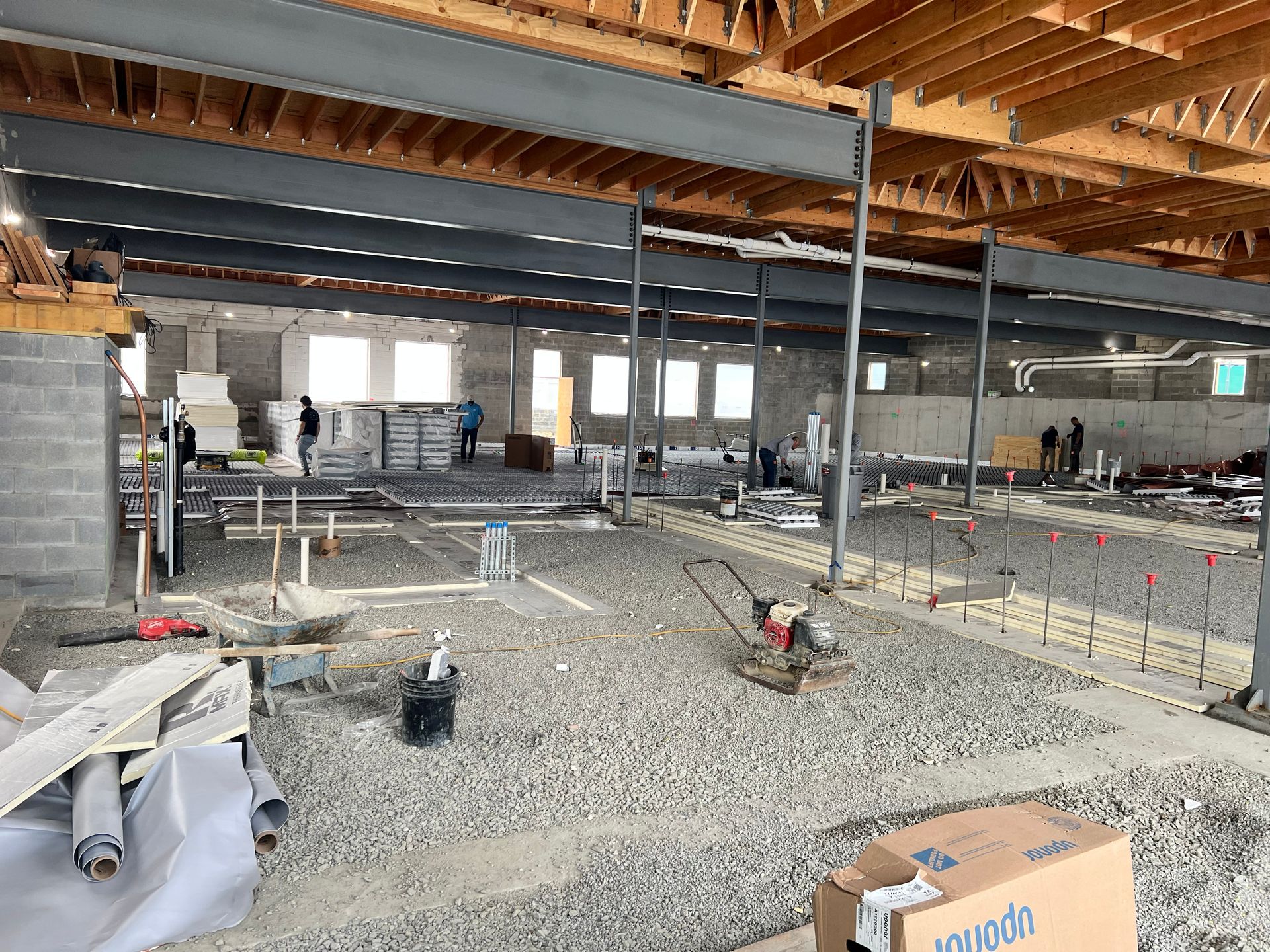 Partially built interior with exposed wooden beams, concrete block walls, and construction materials on gravel floor