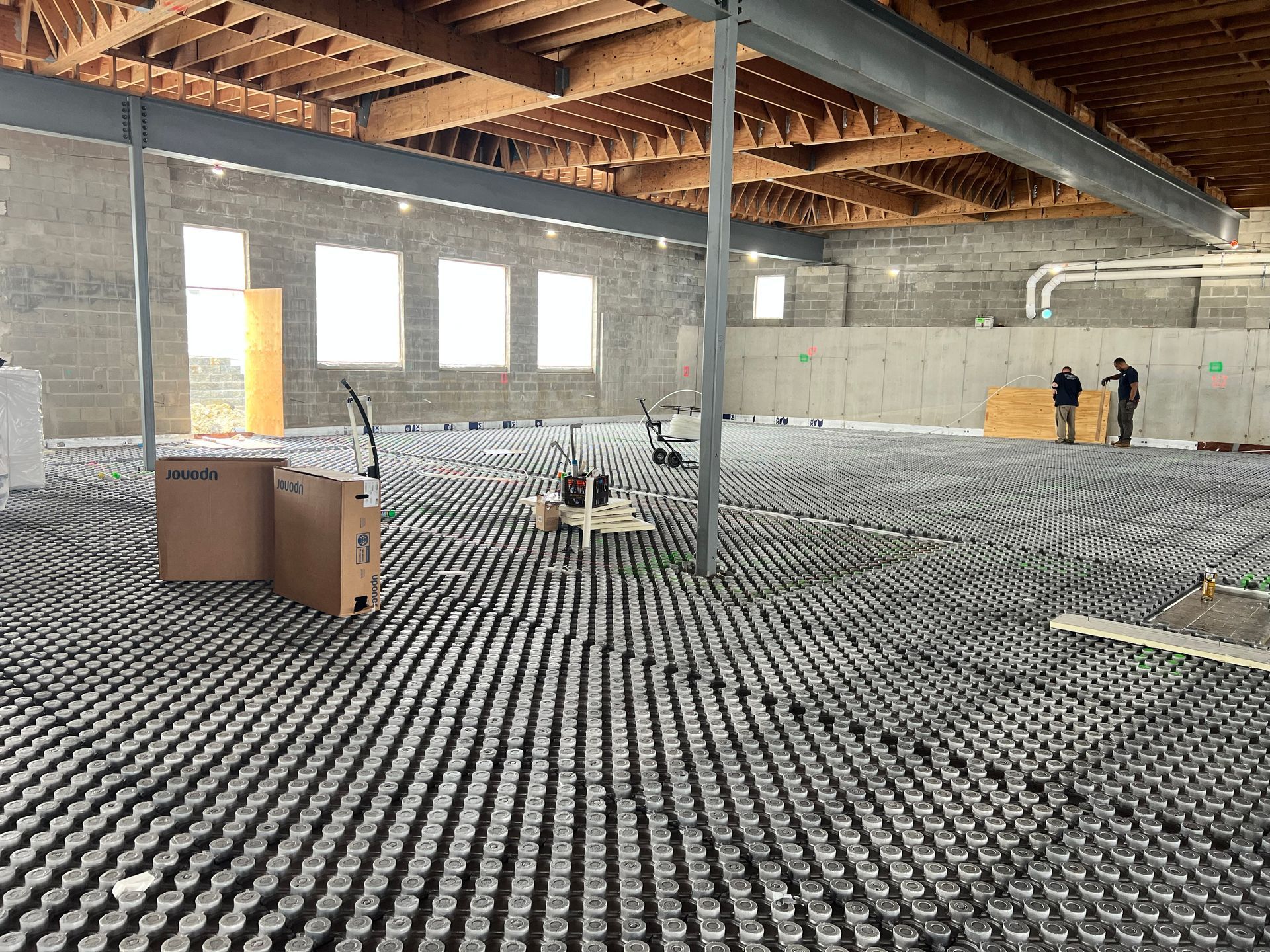 Construction site interior with rows of drainage pods on the floor and workers near the back wall