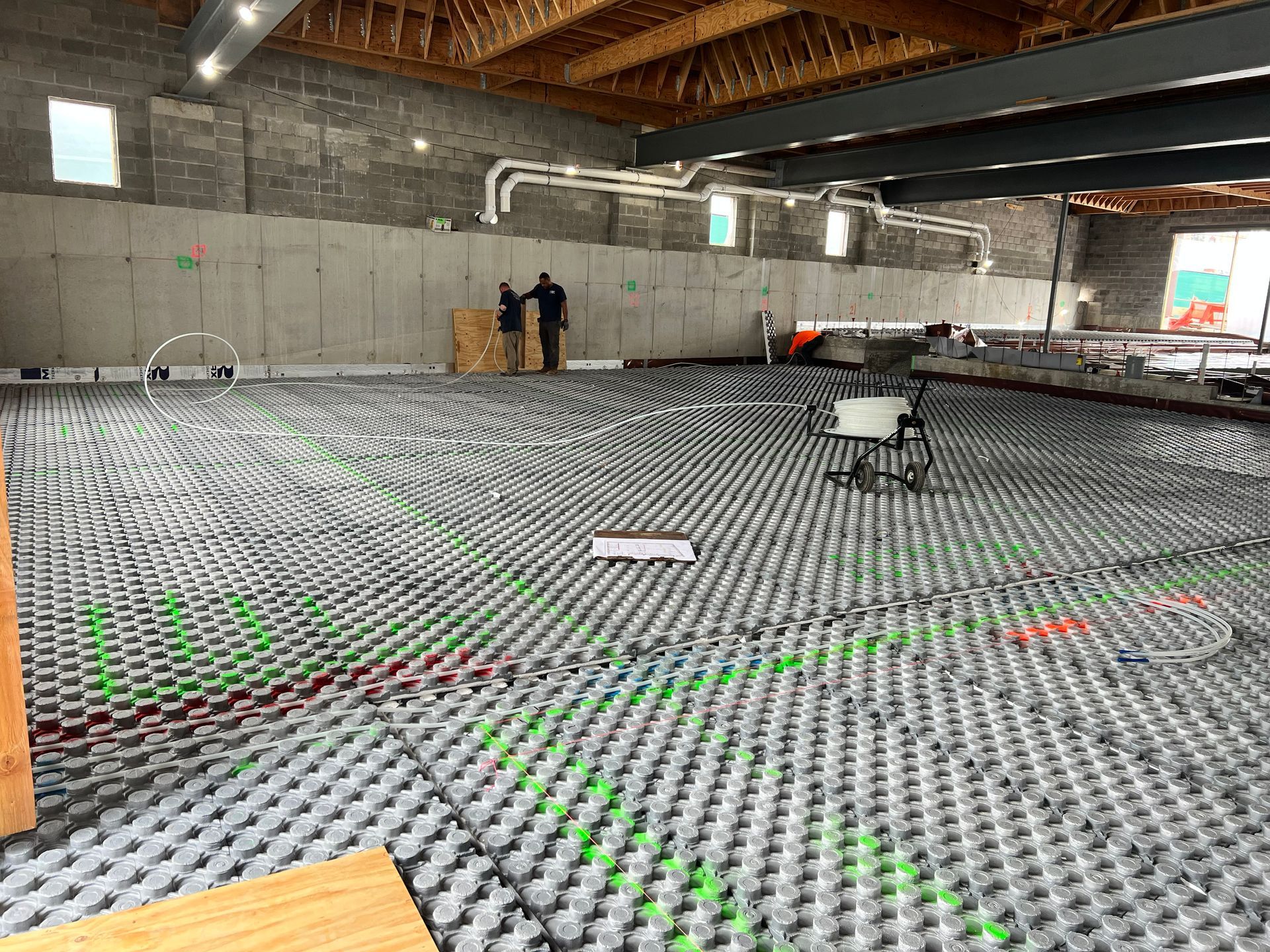 Indoor construction site with workers installing a gray floor over a concrete slab