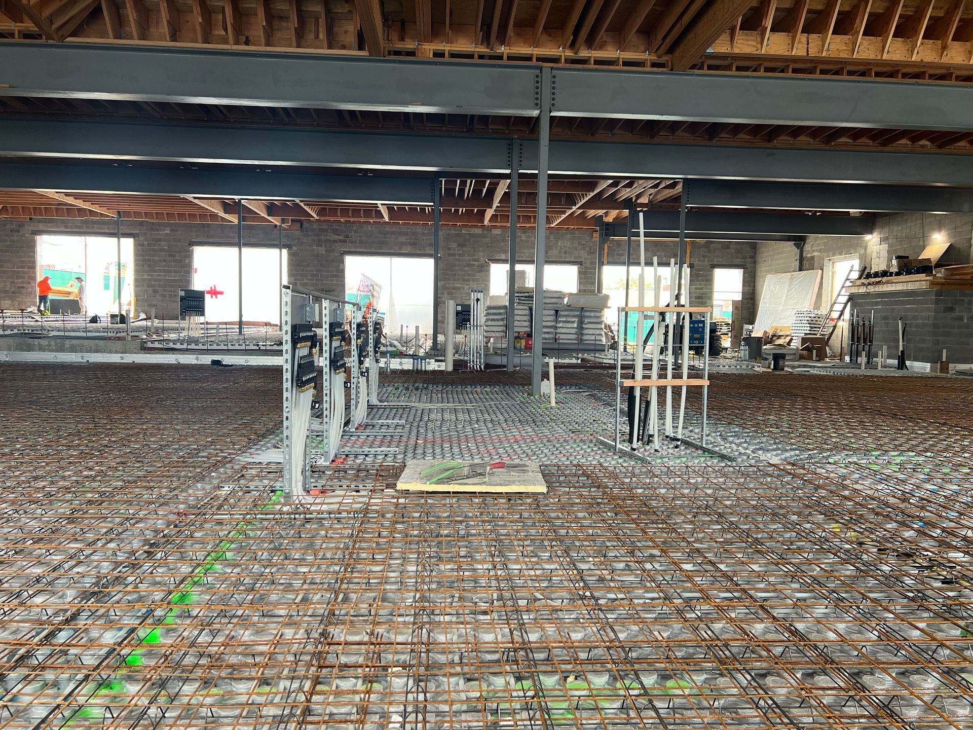 Construction site interior with rebar grid floor, exposed ceiling beams, and vertical pipes under renovation
