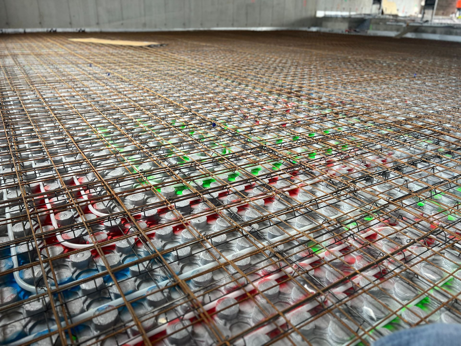 Large concrete floor covered with a dense grid of colorful metal pipes and supports inside a building