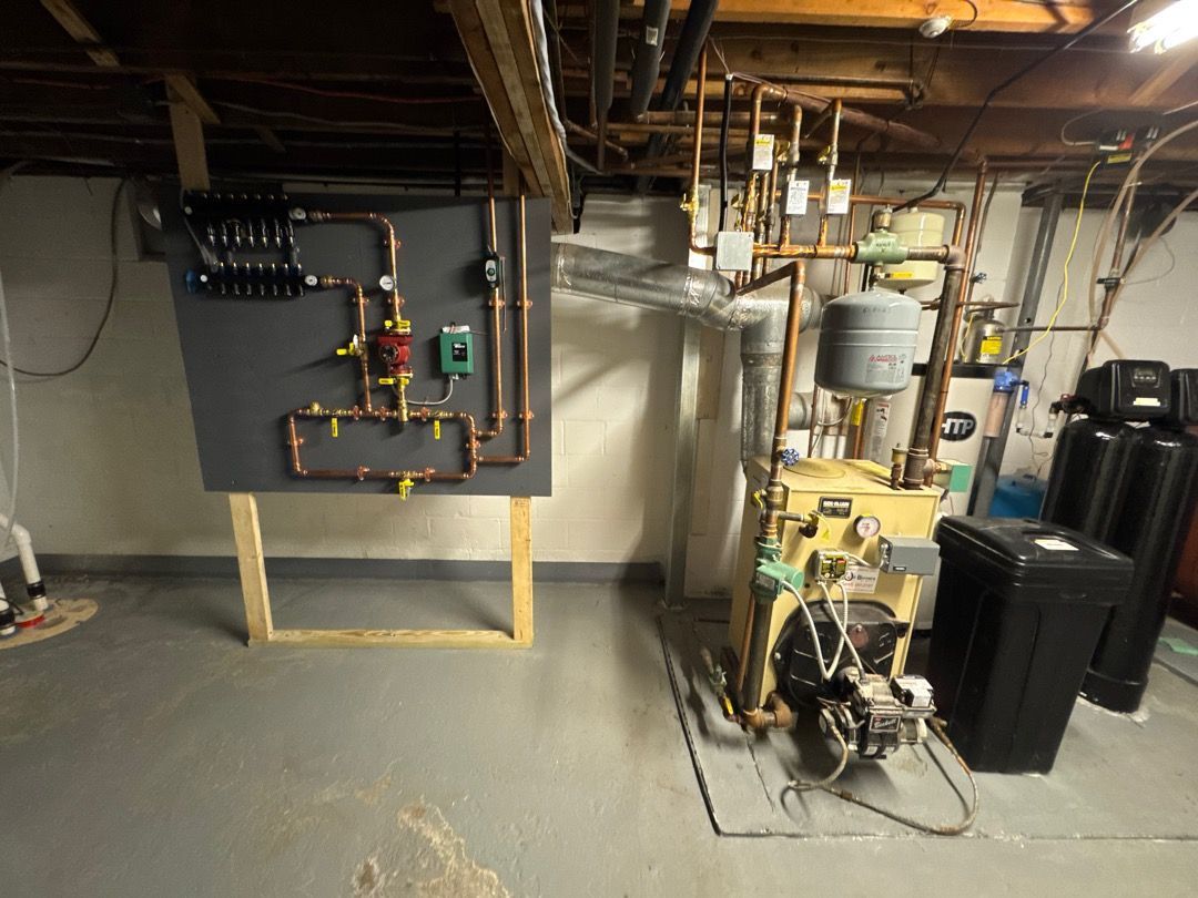 Basement utility room with boiler, pipes, gauges, and two black water tanks.