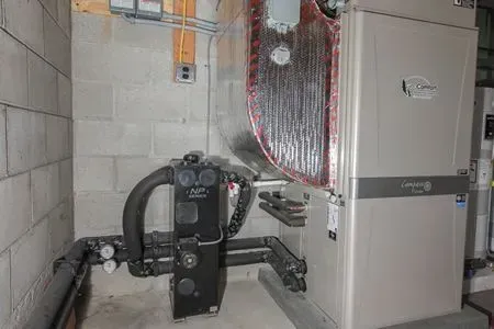 Indoor utility room with a black pump system and a white furnace beside ductwork and pipes