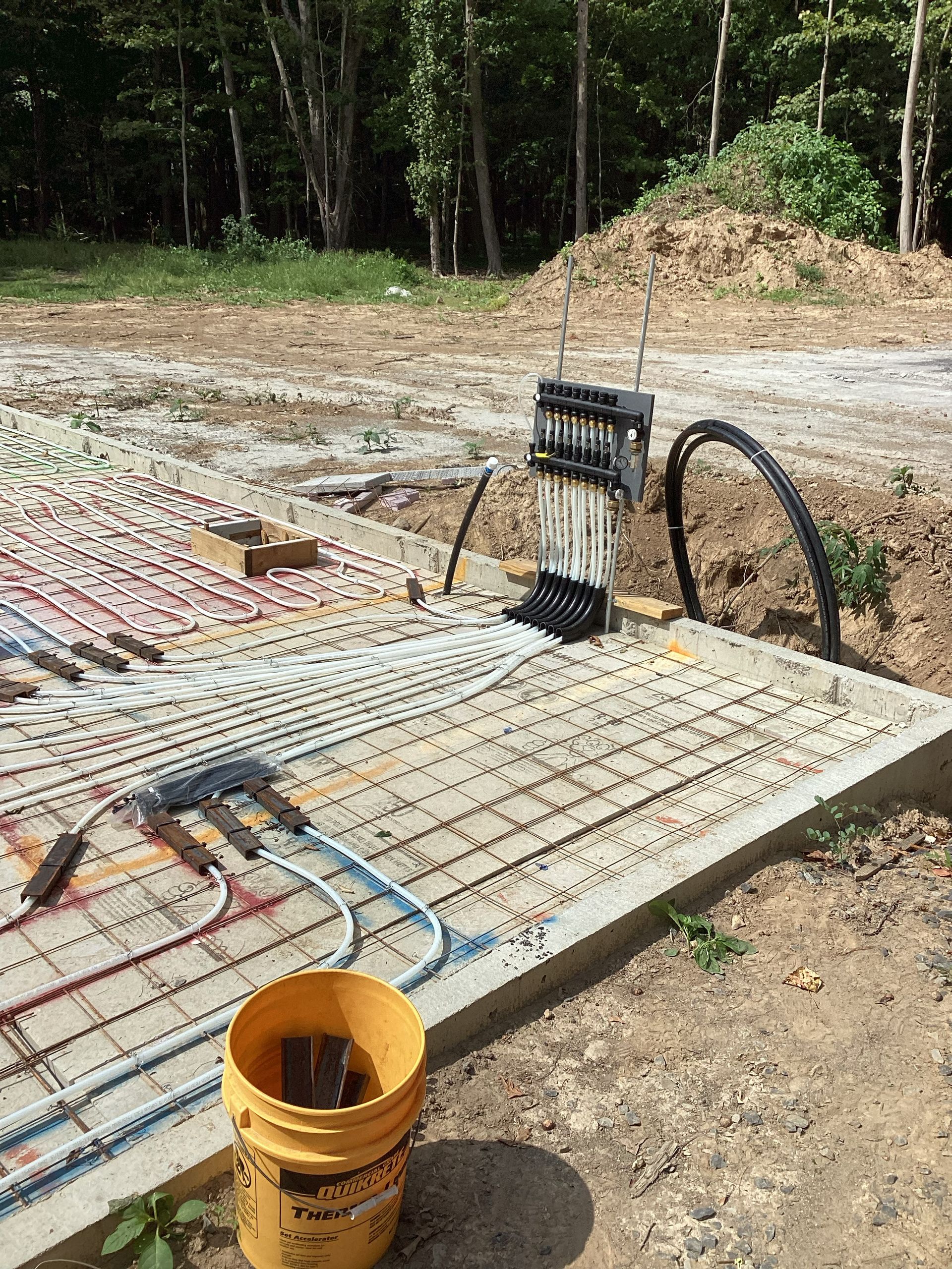 Concrete slab with exposed rebar, electrical conduit, and yellow bucket at a construction site