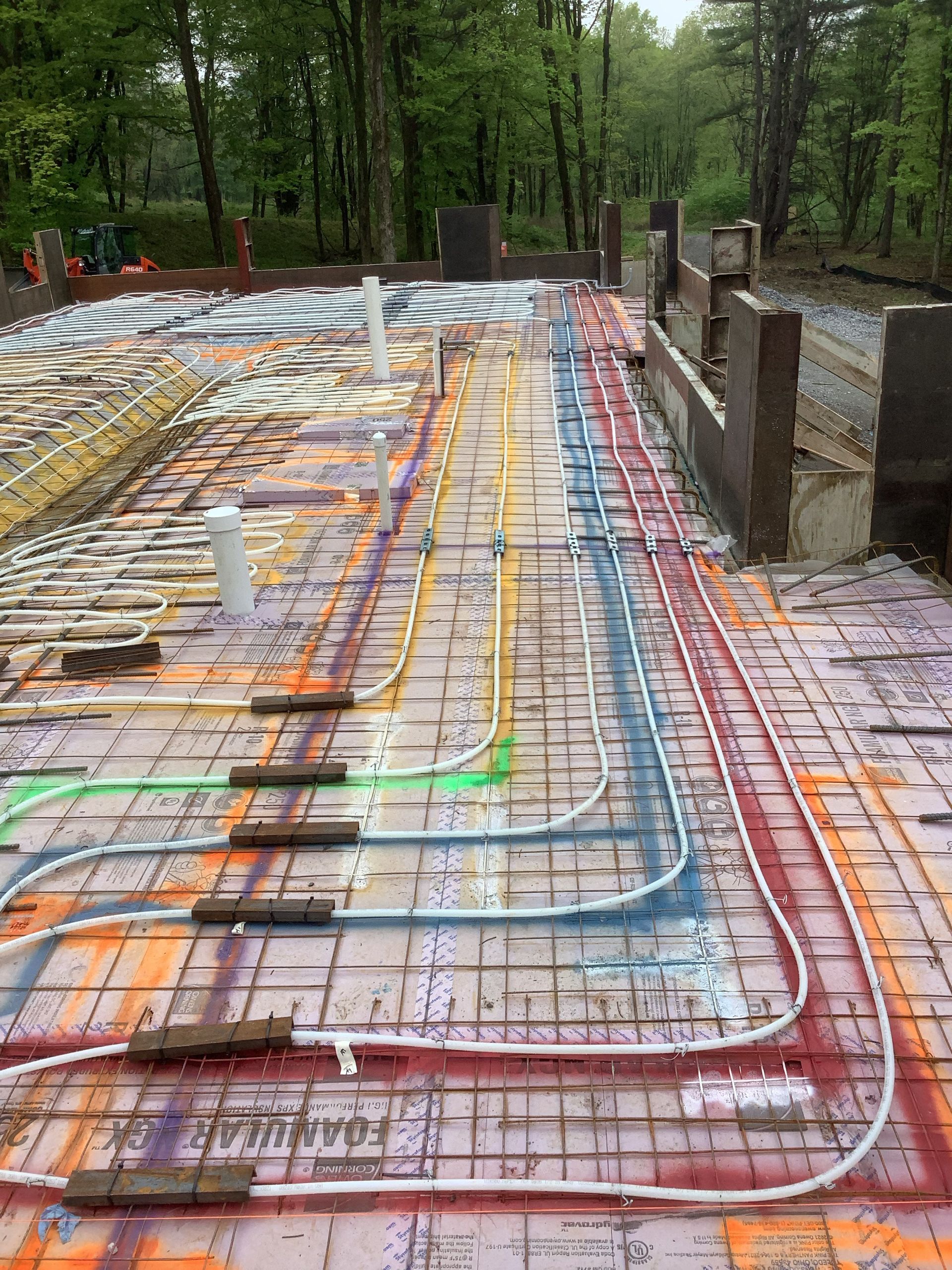 Color-coded radiant floor heating tubes laid over a concrete slab in a wooded outdoor construction site