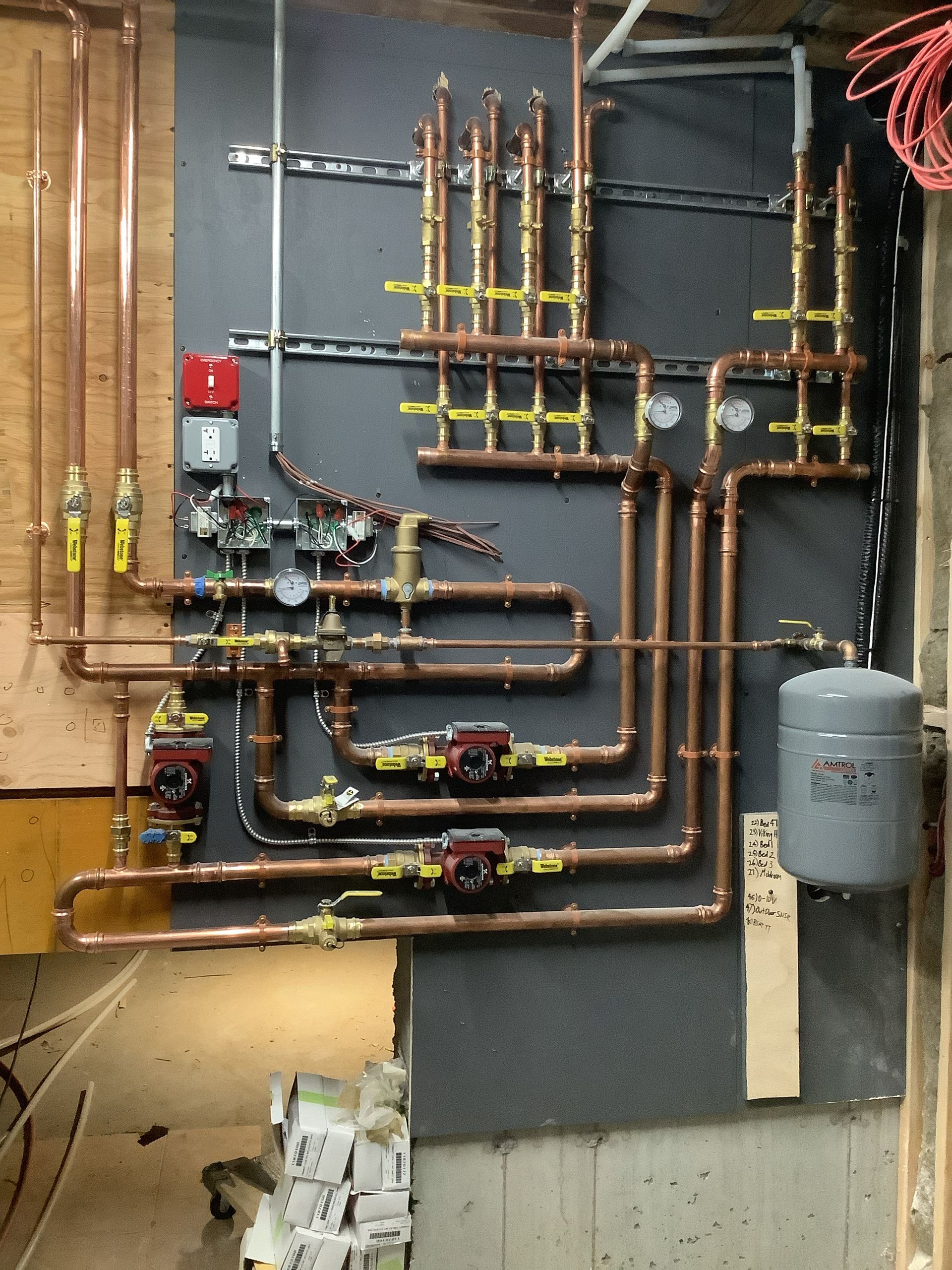 Wall of copper plumbing pipes and valves with a gray expansion tank in a mechanical room