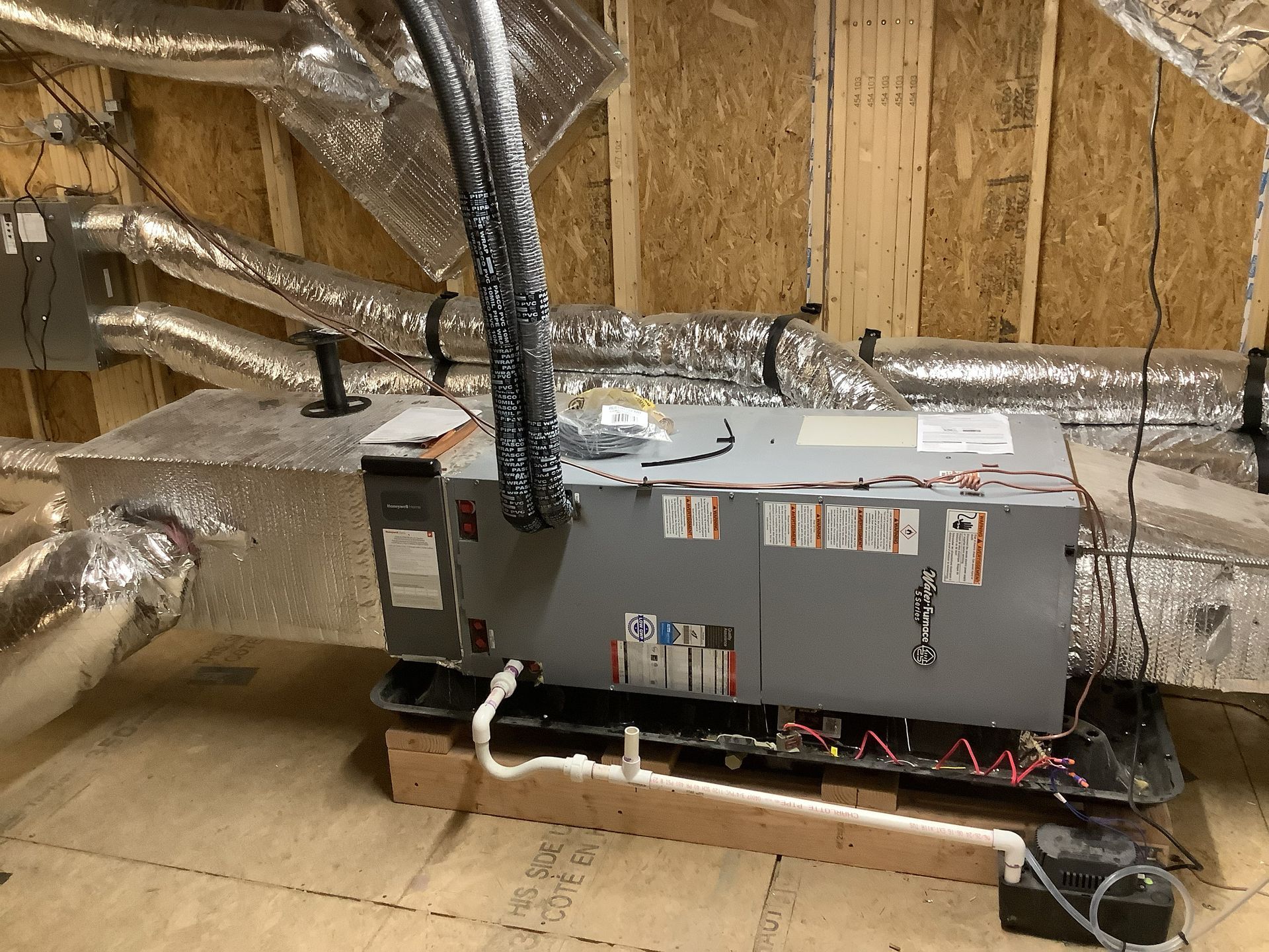 Furnace unit installed in an attic with silver ductwork and exposed wooden rafters.