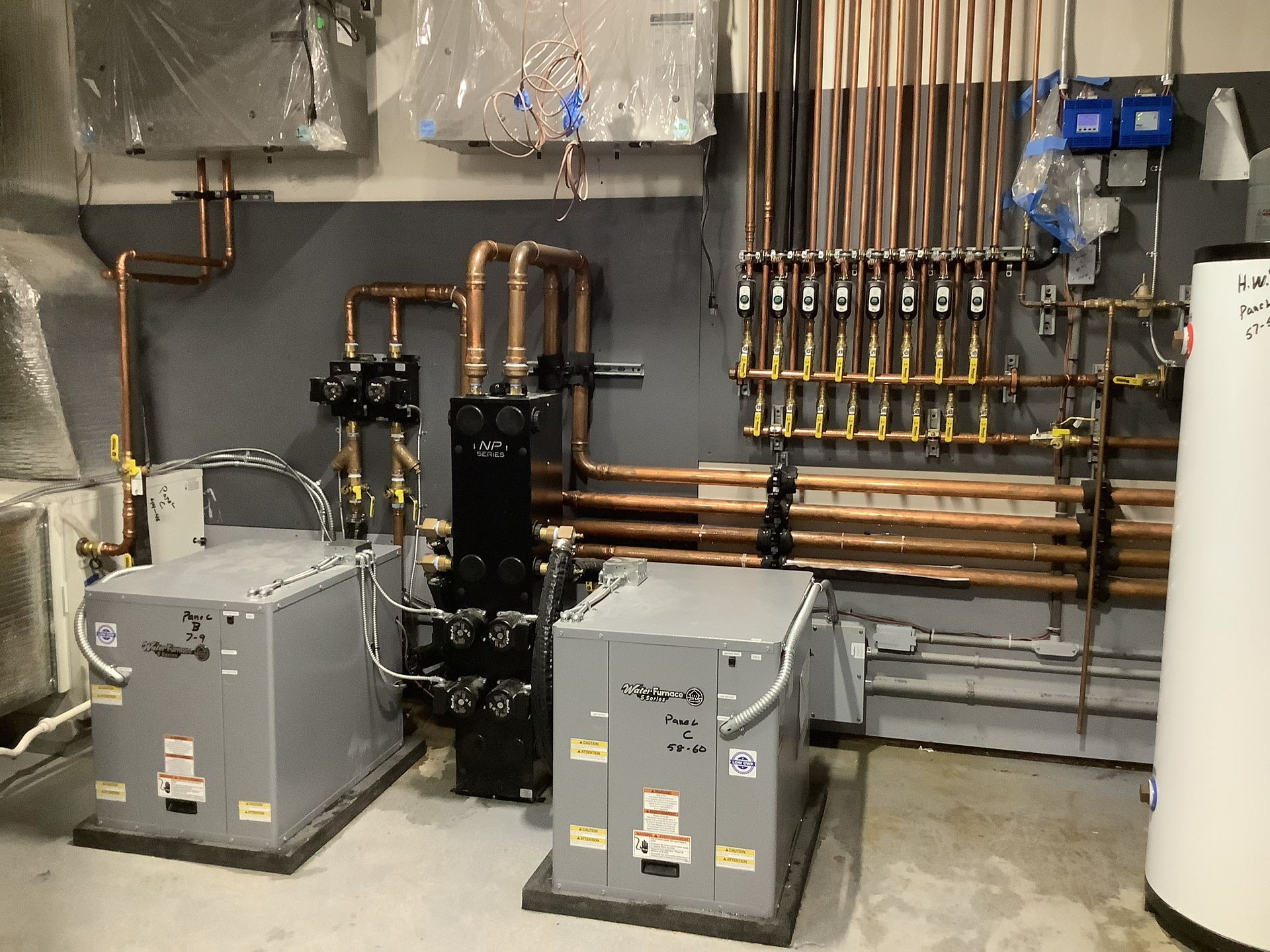 Mechanical room with gray HVAC units, copper pipes, and a white water heater along the wall