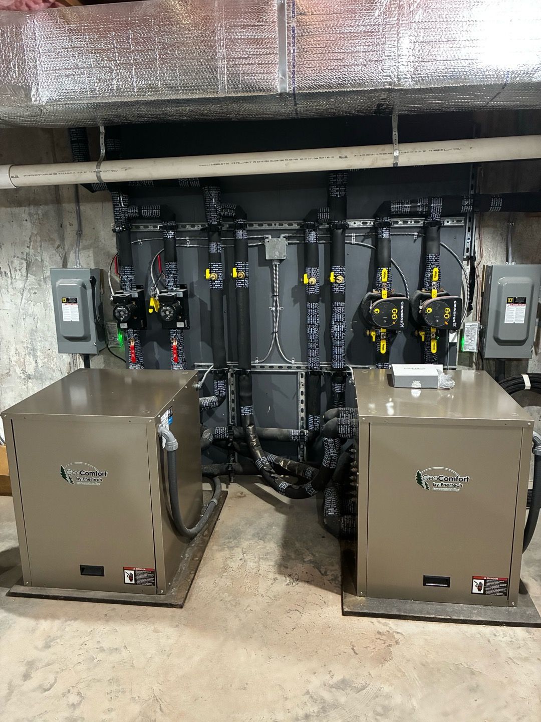 Industrial equipment room with two beige HVAC units in front of a wall of black pumps and pipes