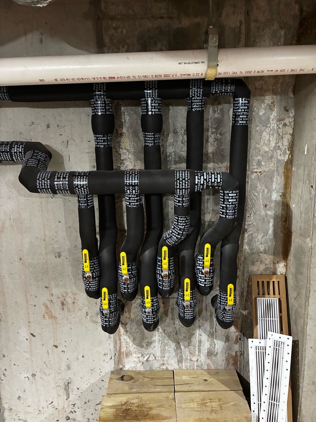 Insulated black pipes and valves in a utility room, labeled with yellow tags under a white overhead pipe