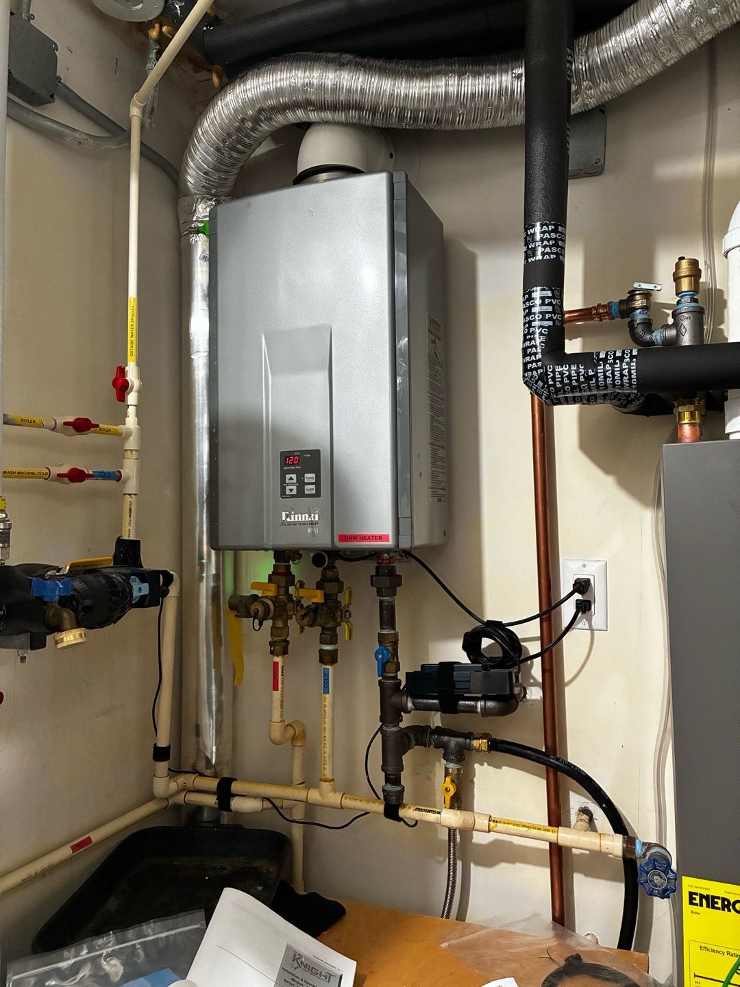 Wall-mounted water heater with pipes and ducting in a utility closet, with a small gauge on the front.