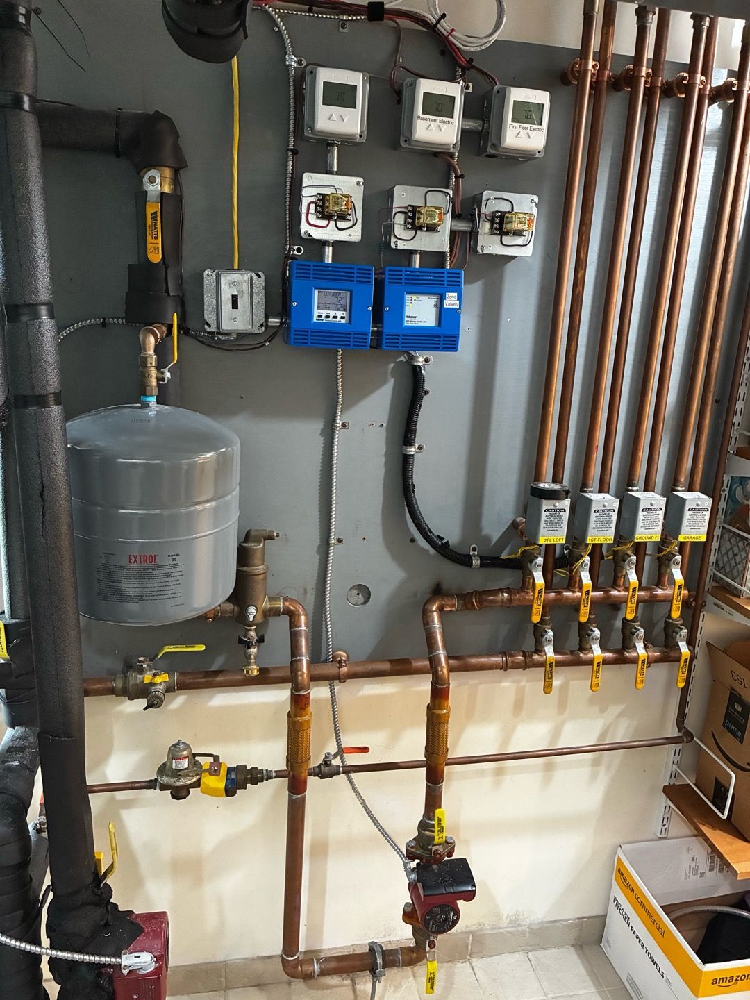 Utility room with copper pipes, valves, meters, and a gray water tank mounted on the wall.