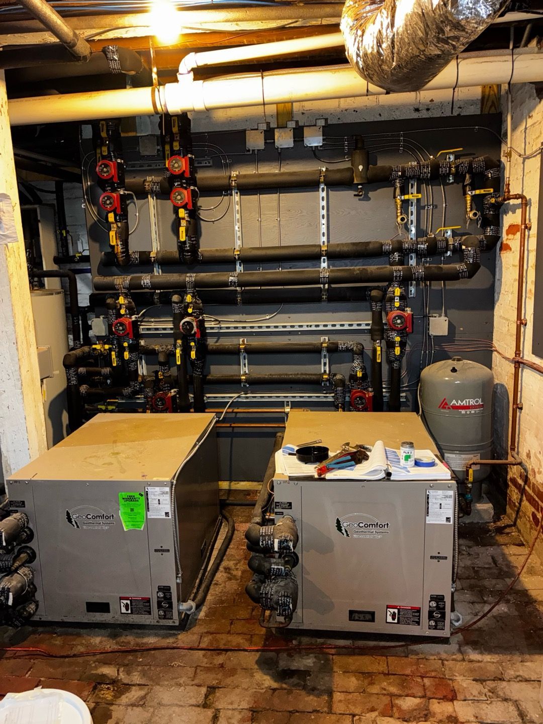 Basement mechanical room with two HVAC units, pipes, and ductwork.