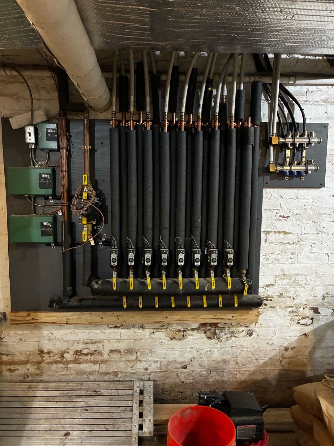 Industrial wall with black pipes, valves, and electrical boxes in a basement utility room
