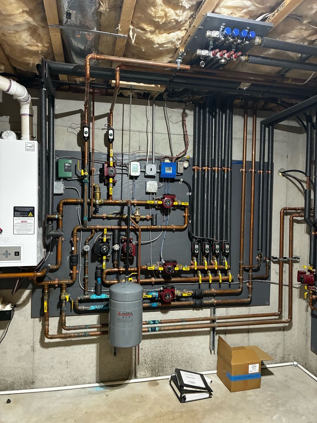 Wall-mounted plumbing and heating pipes, valves, and control boxes in a utility room.