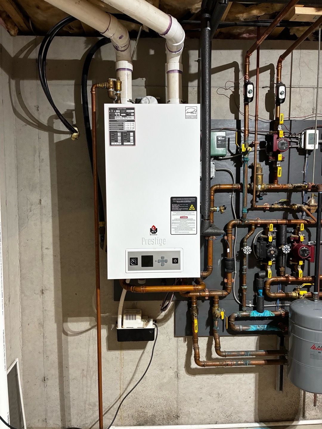White wall-mounted boiler with exposed pipes and valves in a utility room on a concrete wall