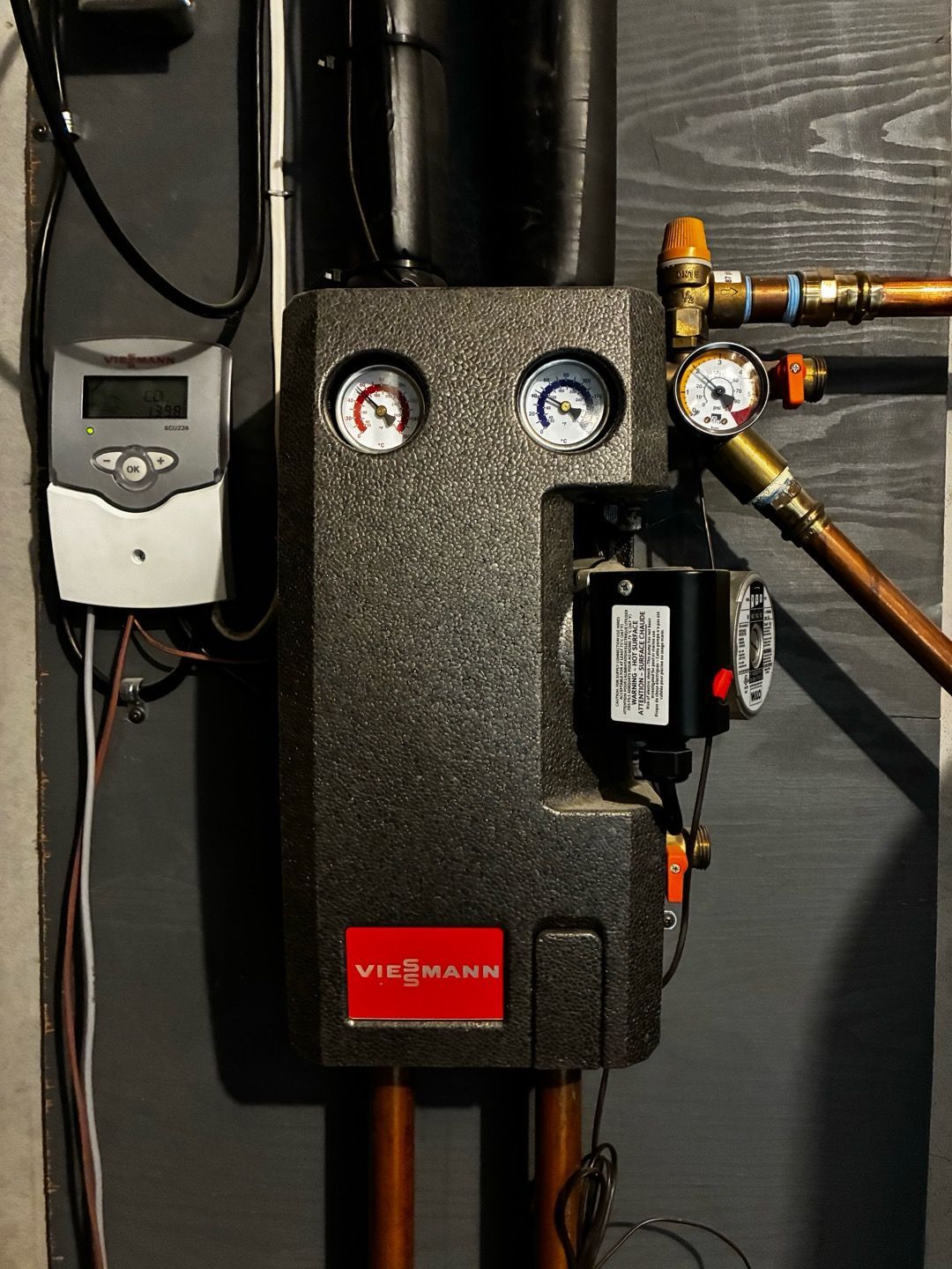 Wall-mounted boiler with gauges, valves, and pipes on a dark wall