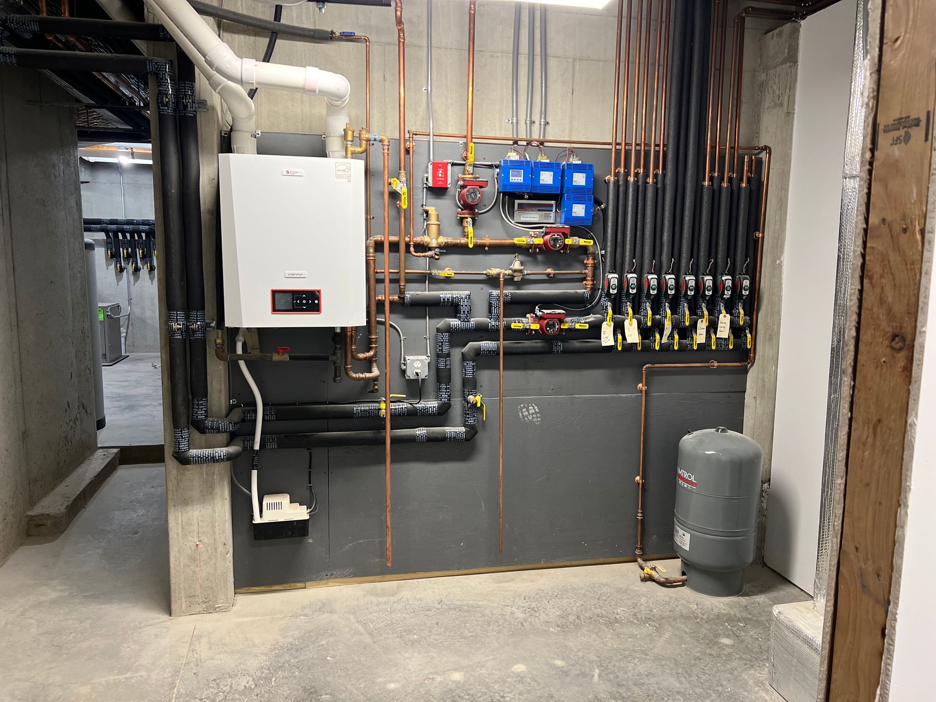 Basement utility room with boiler, pipes, electrical panels, and water heater on concrete walls