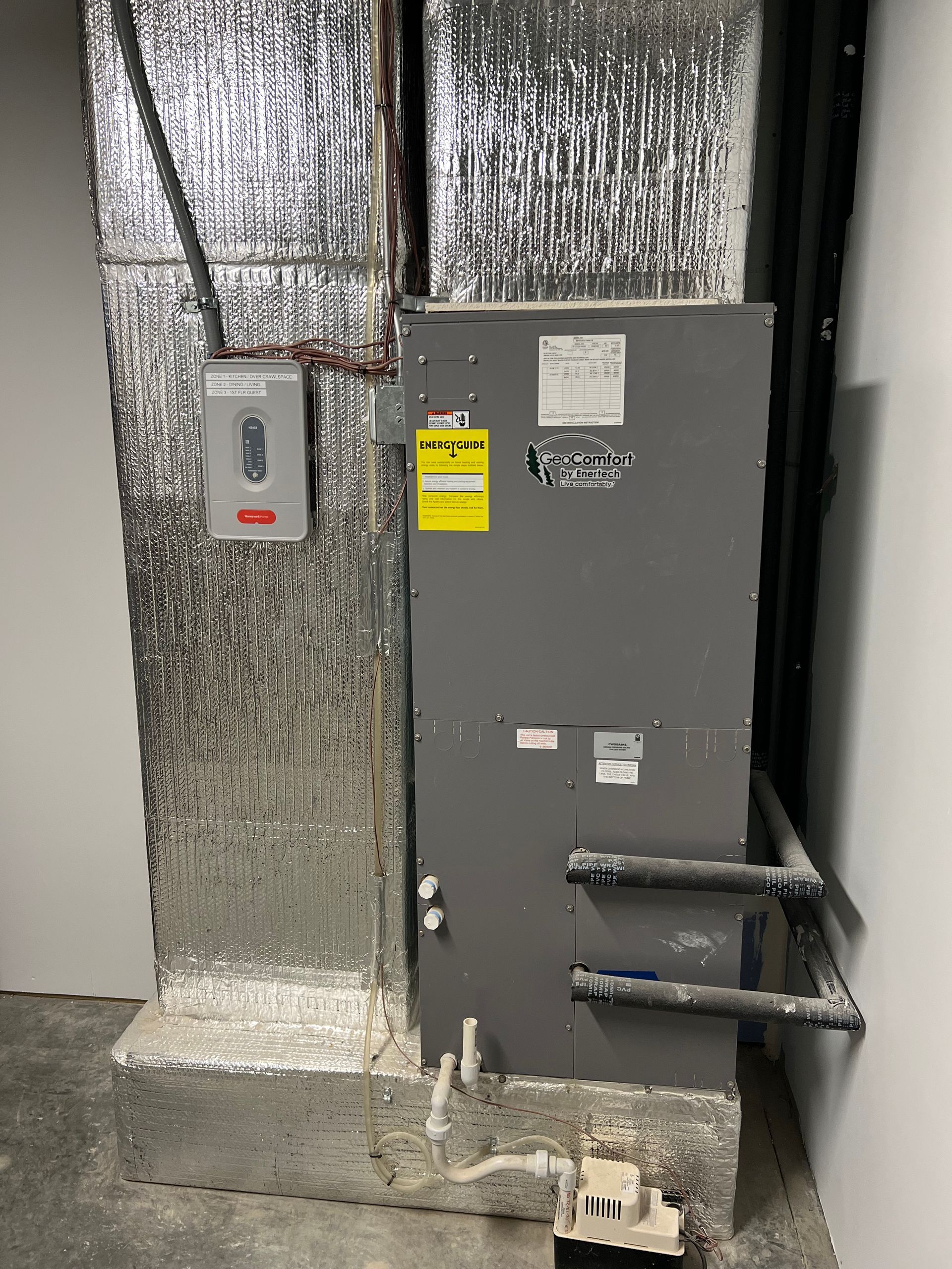 Gray industrial electrical cabinet beside insulated wall panels with two pipes and a nearby wall switch box