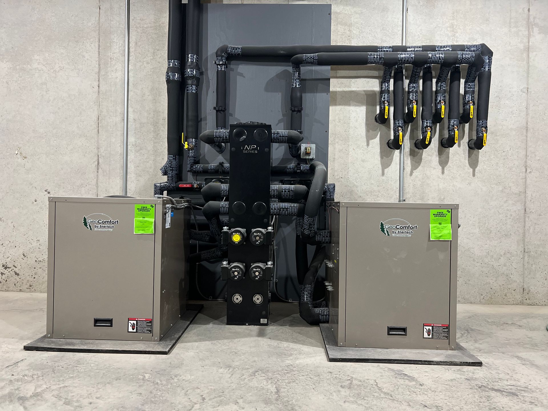 Two gray industrial pump cabinets with black piping and valves mounted against a concrete wall.