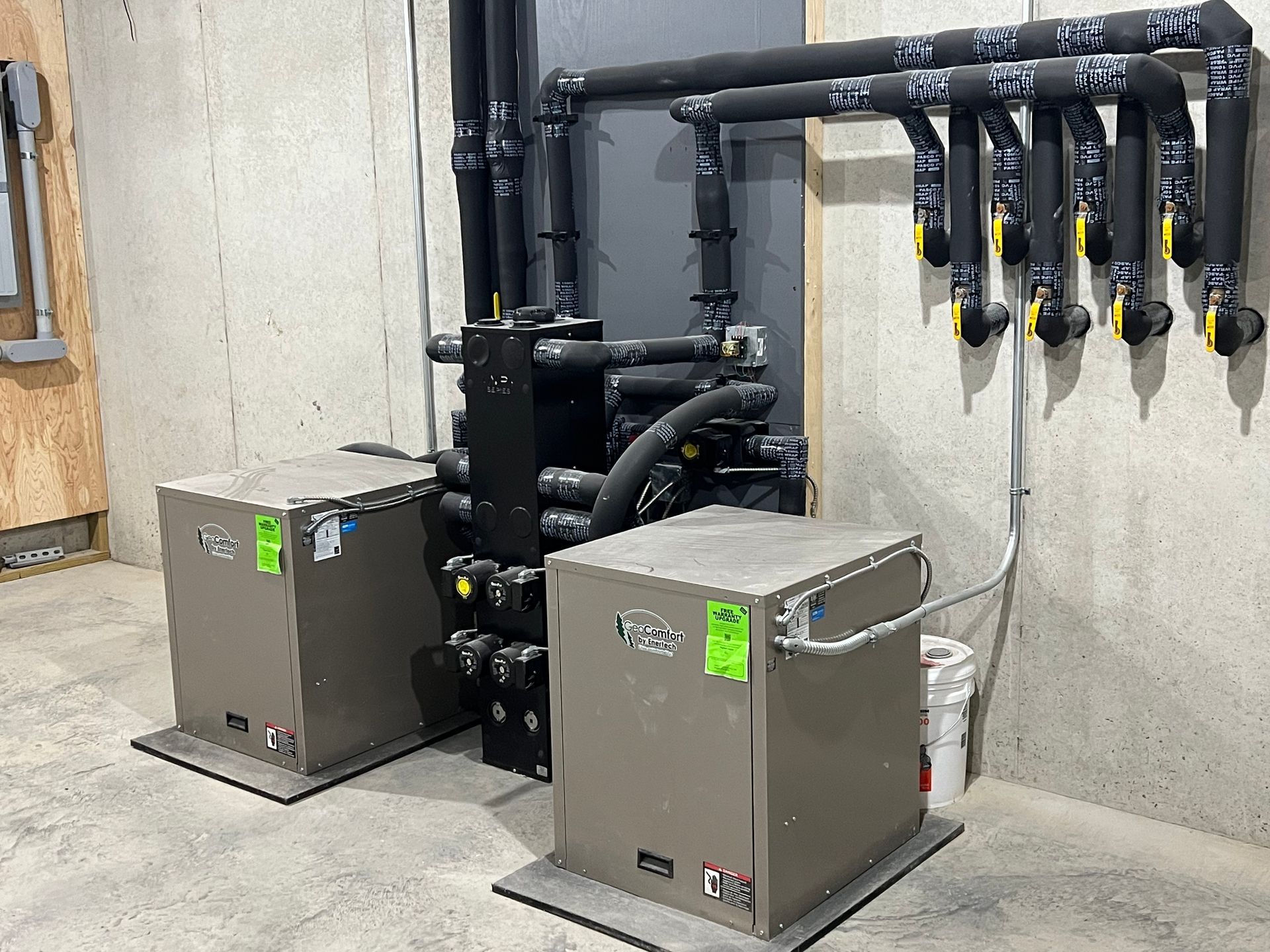Industrial equipment room with two metal pumps, black piping, and wall-mounted valves on a concrete floor