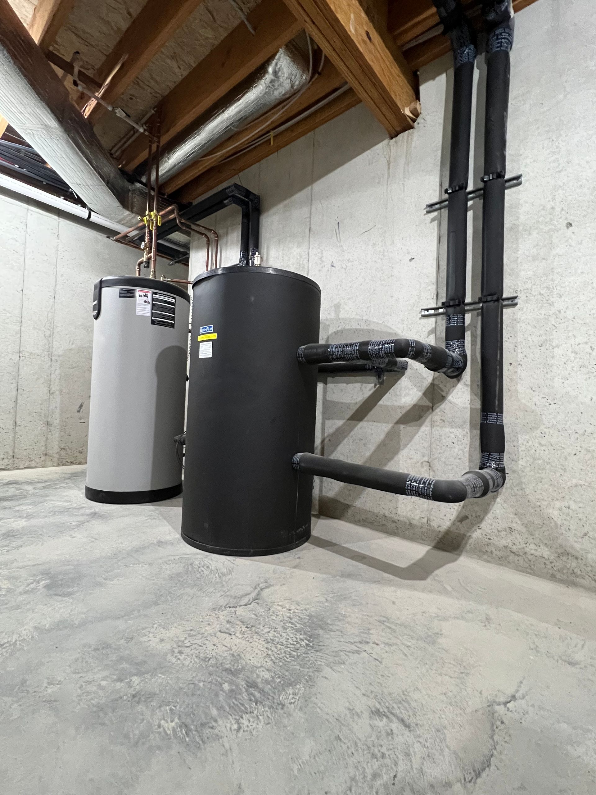 Basement utility room with two large water tanks, exposed pipes, and concrete floor.