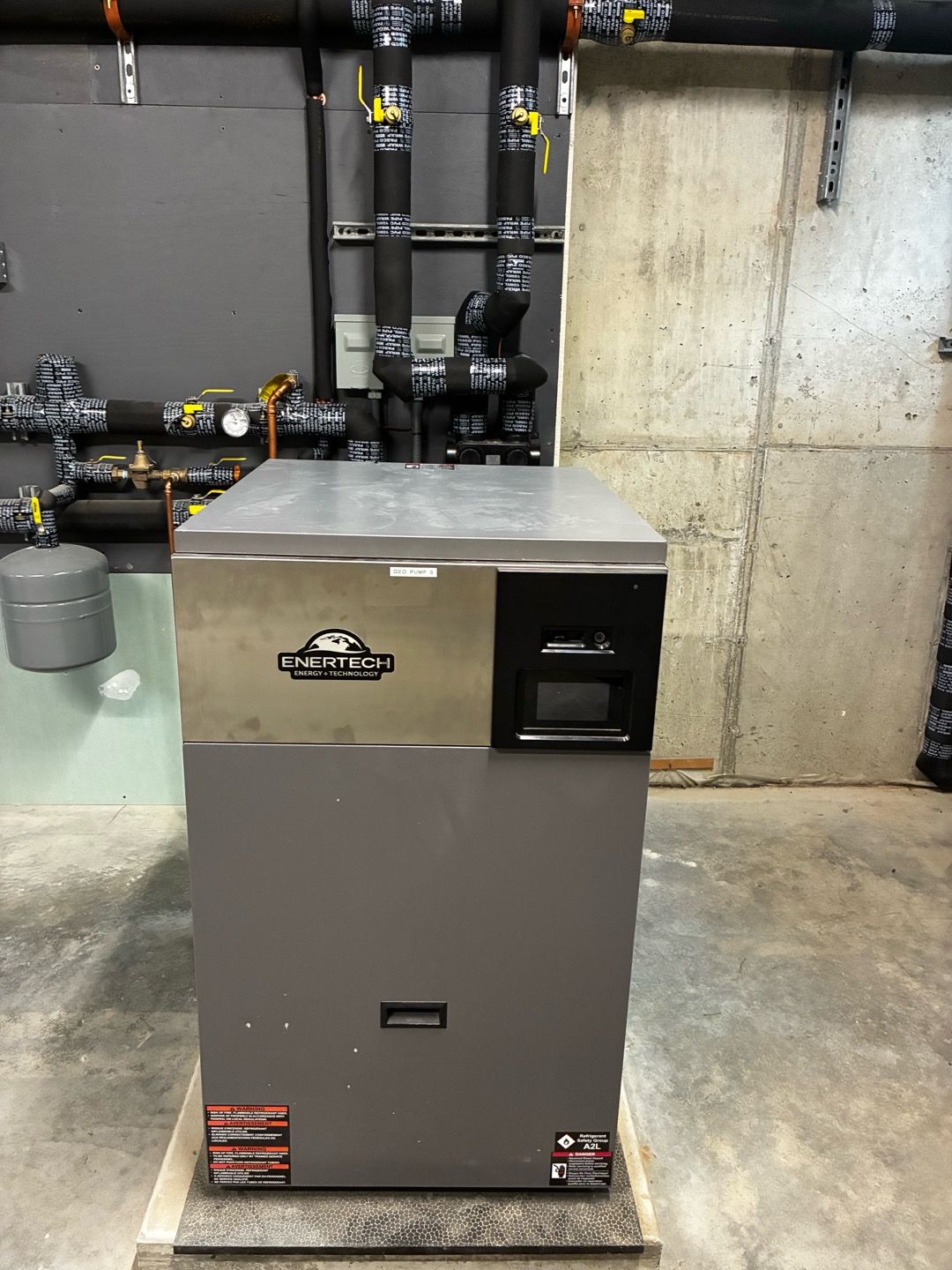 Gray industrial boiler or furnace in a basement against exposed pipes and concrete wall