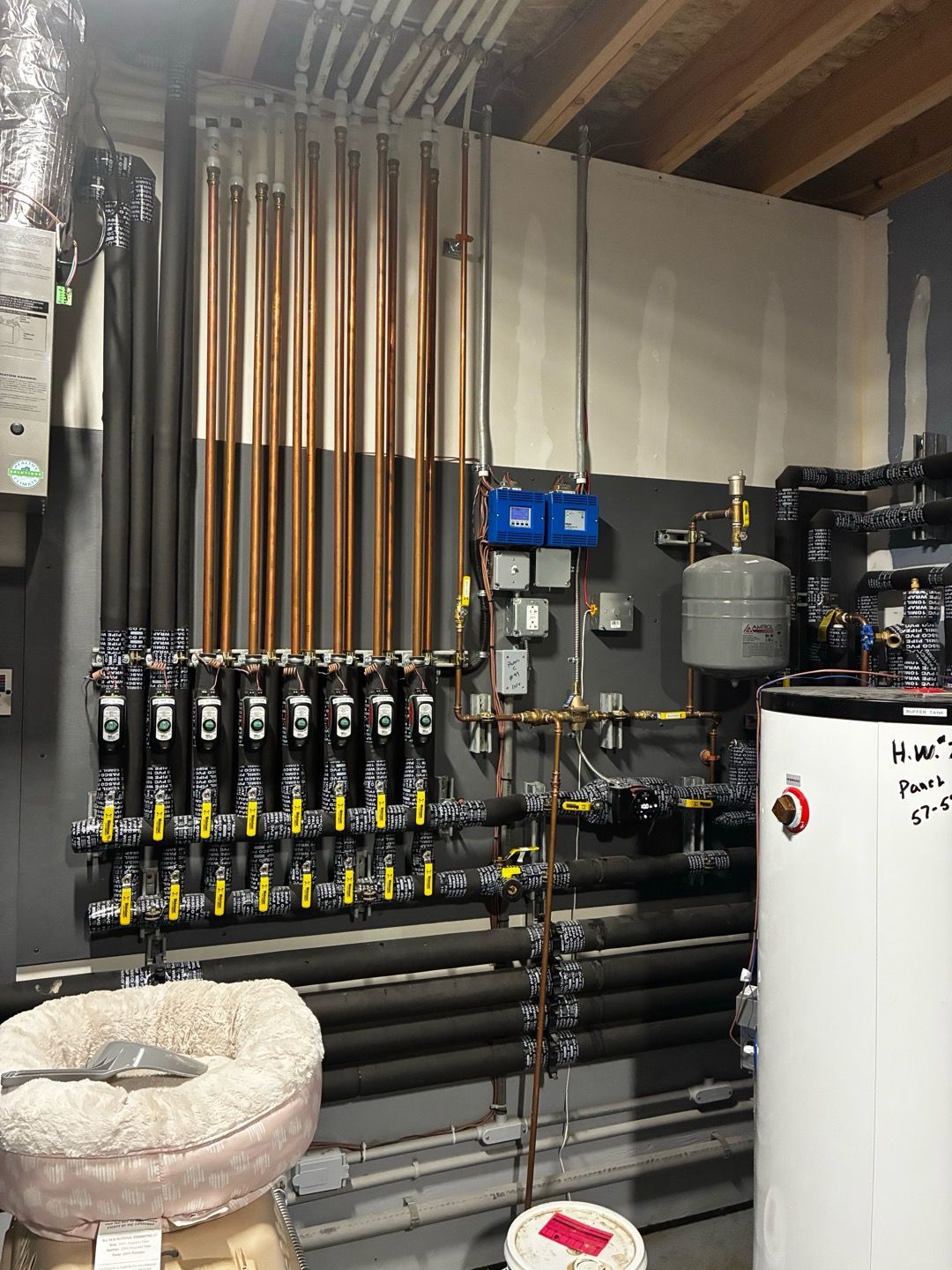 Mechanical room with copper and black pipes, valves, gauges, and a white water heater tank