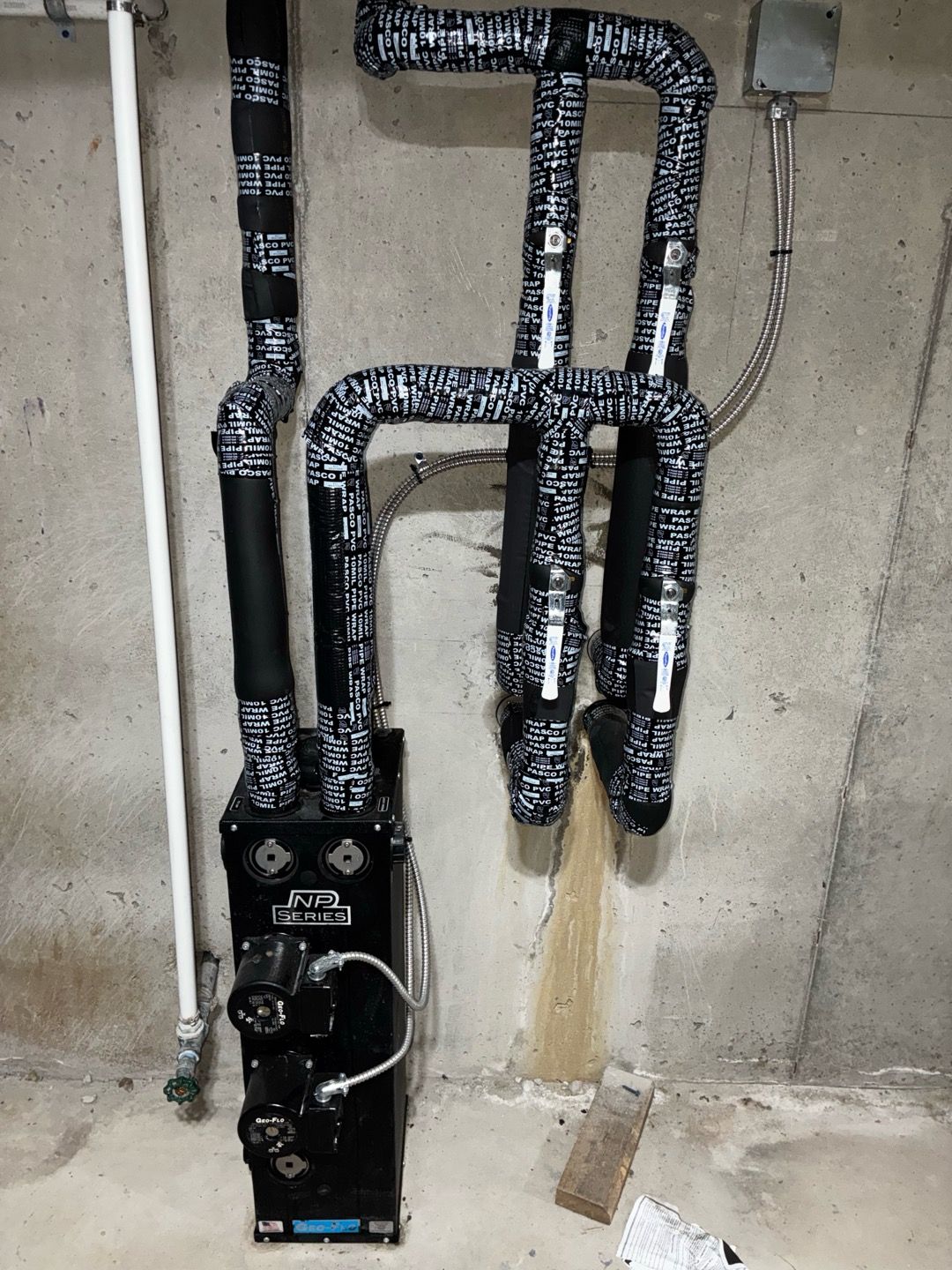 Black water heater and insulated pipes in a basement utility area with concrete wall.