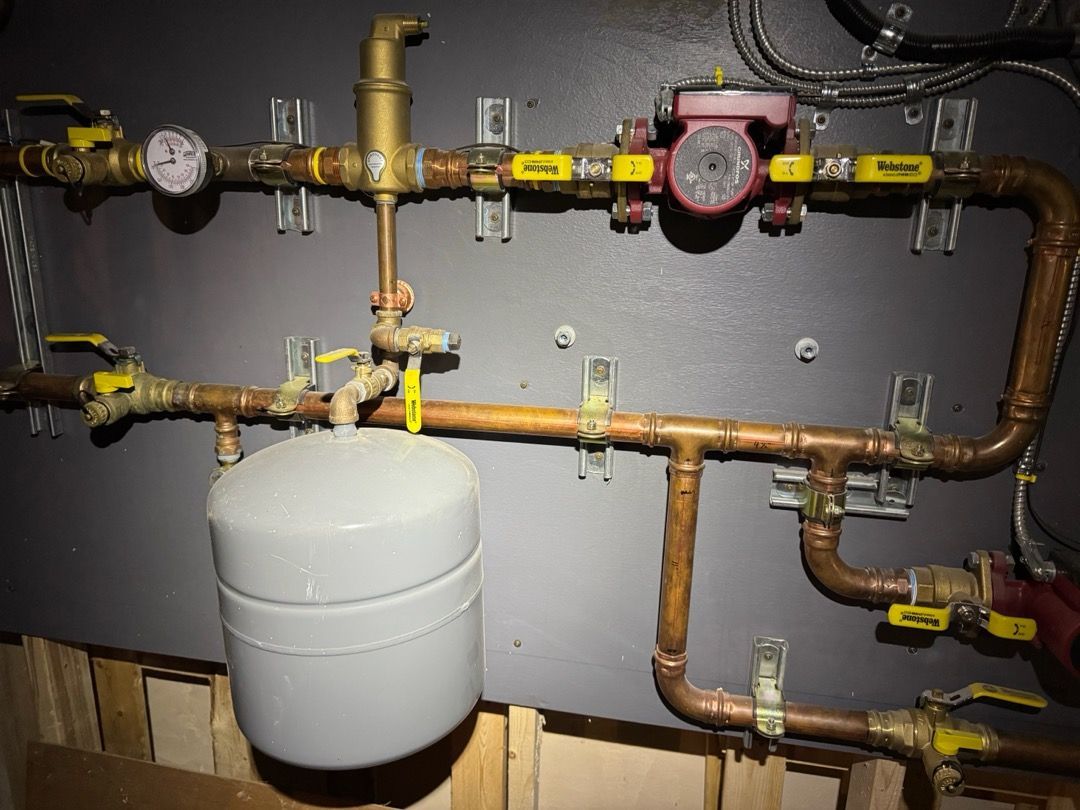 Boiler room pipes and valves with a white expansion tank and red circulation pump on a gray wall