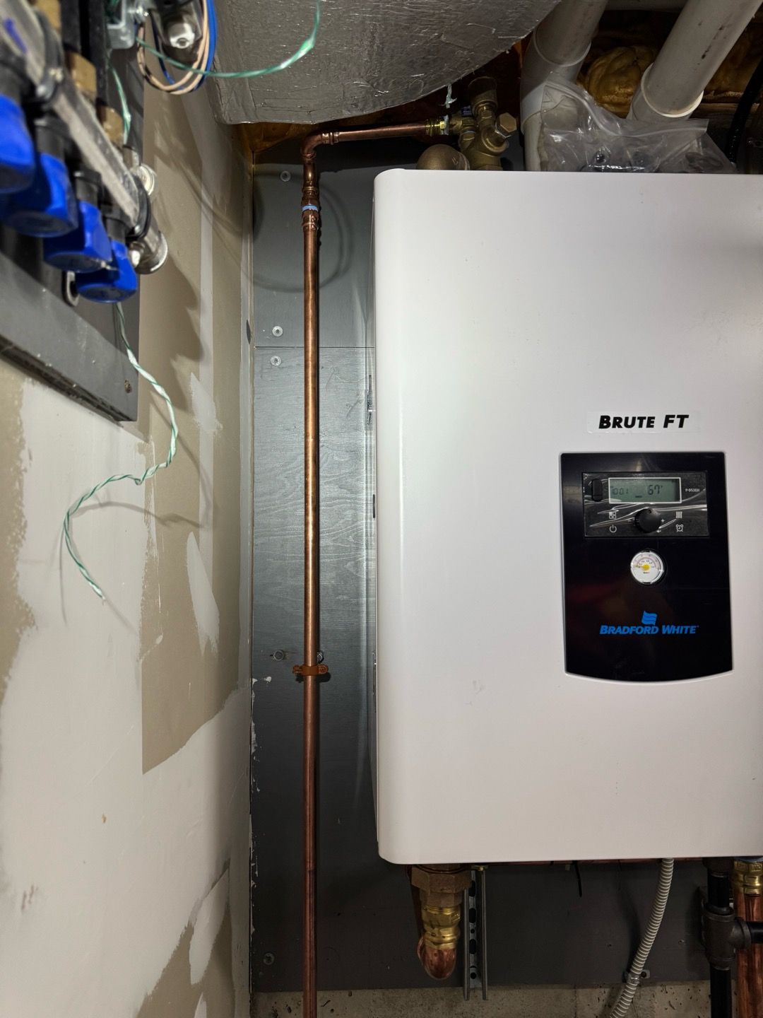 White wall-mounted boiler in a utility closet with exposed pipes and wiring.
