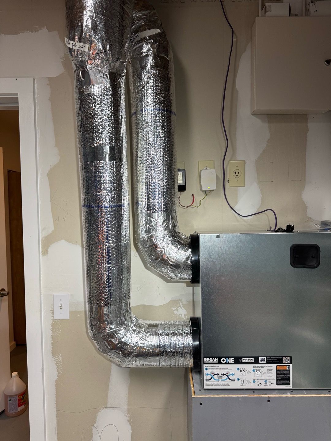 Foil-wrapped HVAC ducts beside a gray furnace in a basement wall area