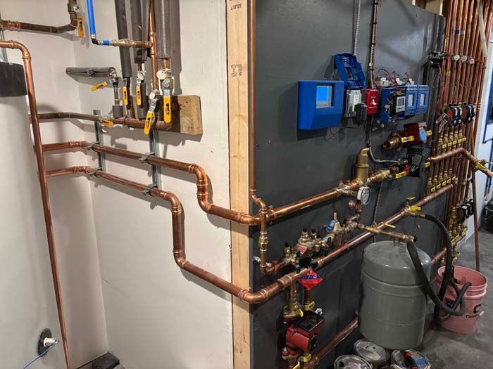 Copper plumbing pipes and valves installed on a basement wall next to a blue boiler unit.