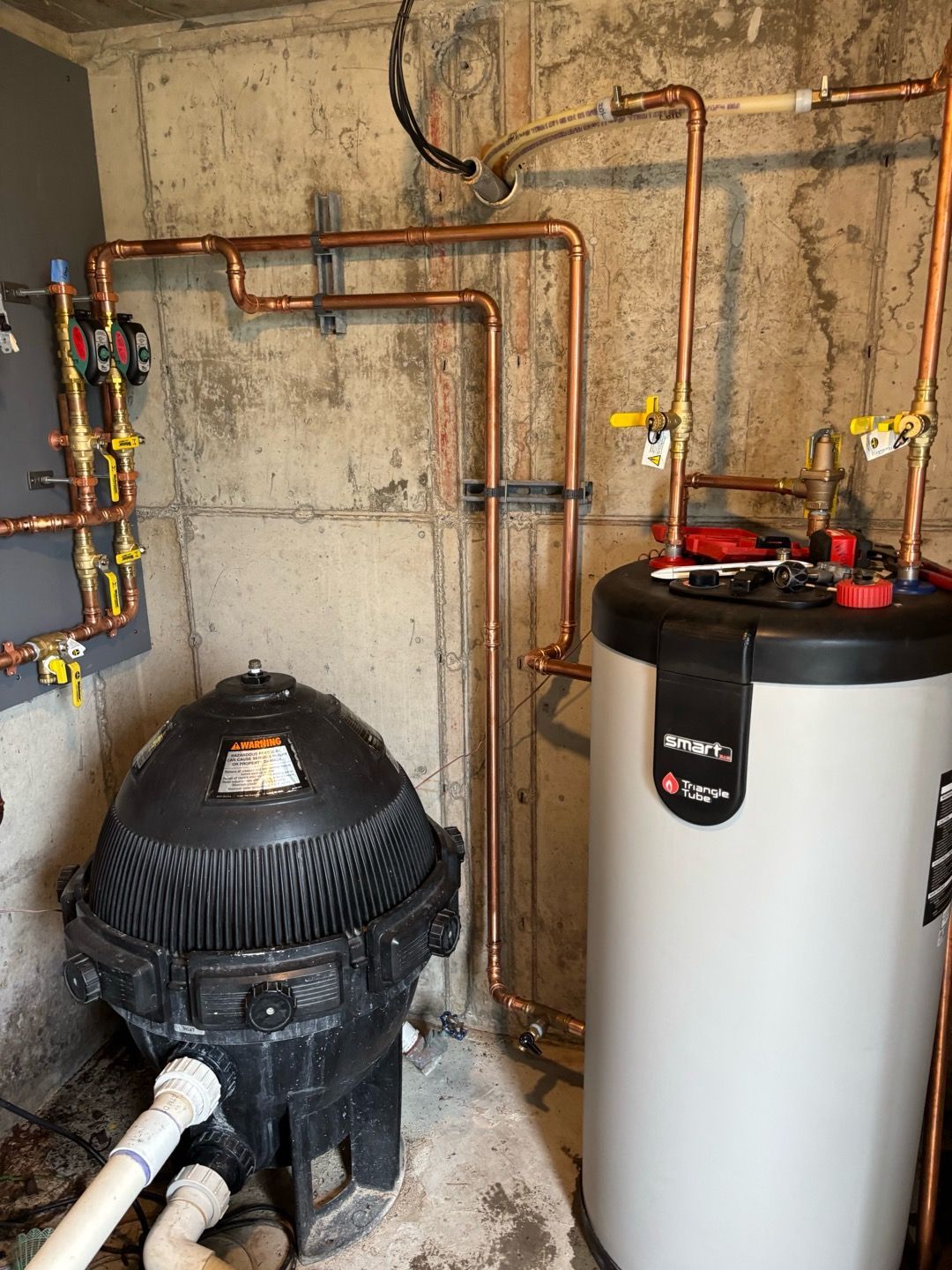 Basement utility area with water heater, black tank, and exposed copper piping on concrete walls