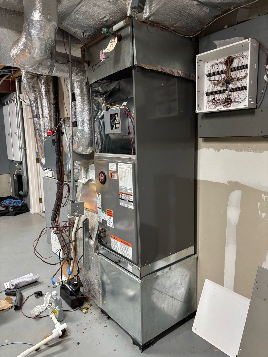 Utility room with furnace, exposed ducts, electrical panels, and tools on the floor.