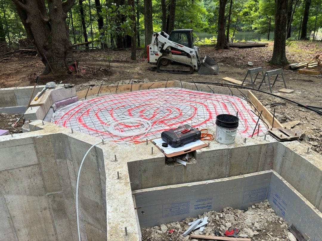 Circular concrete foundation in wooded area, with red chalk markings and a small excavator nearby