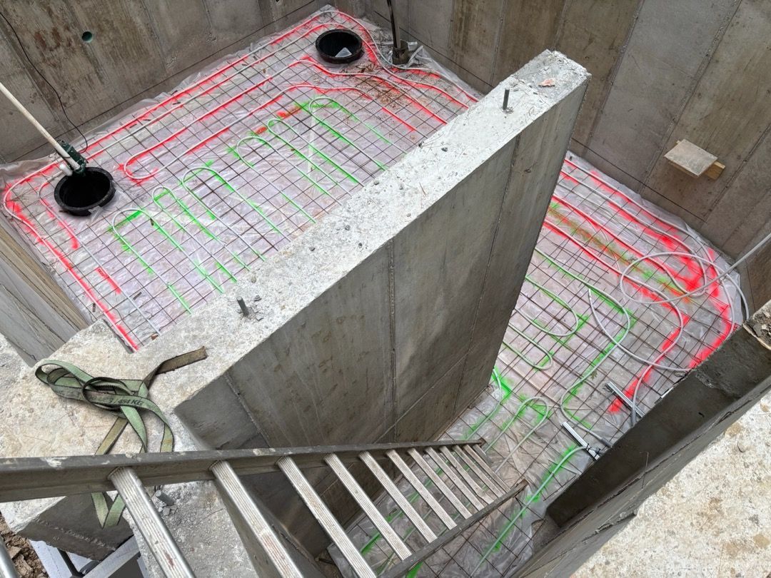 Concrete stairwell with pink and green marked slab, black pipe openings, and a ladder descending into a shaft