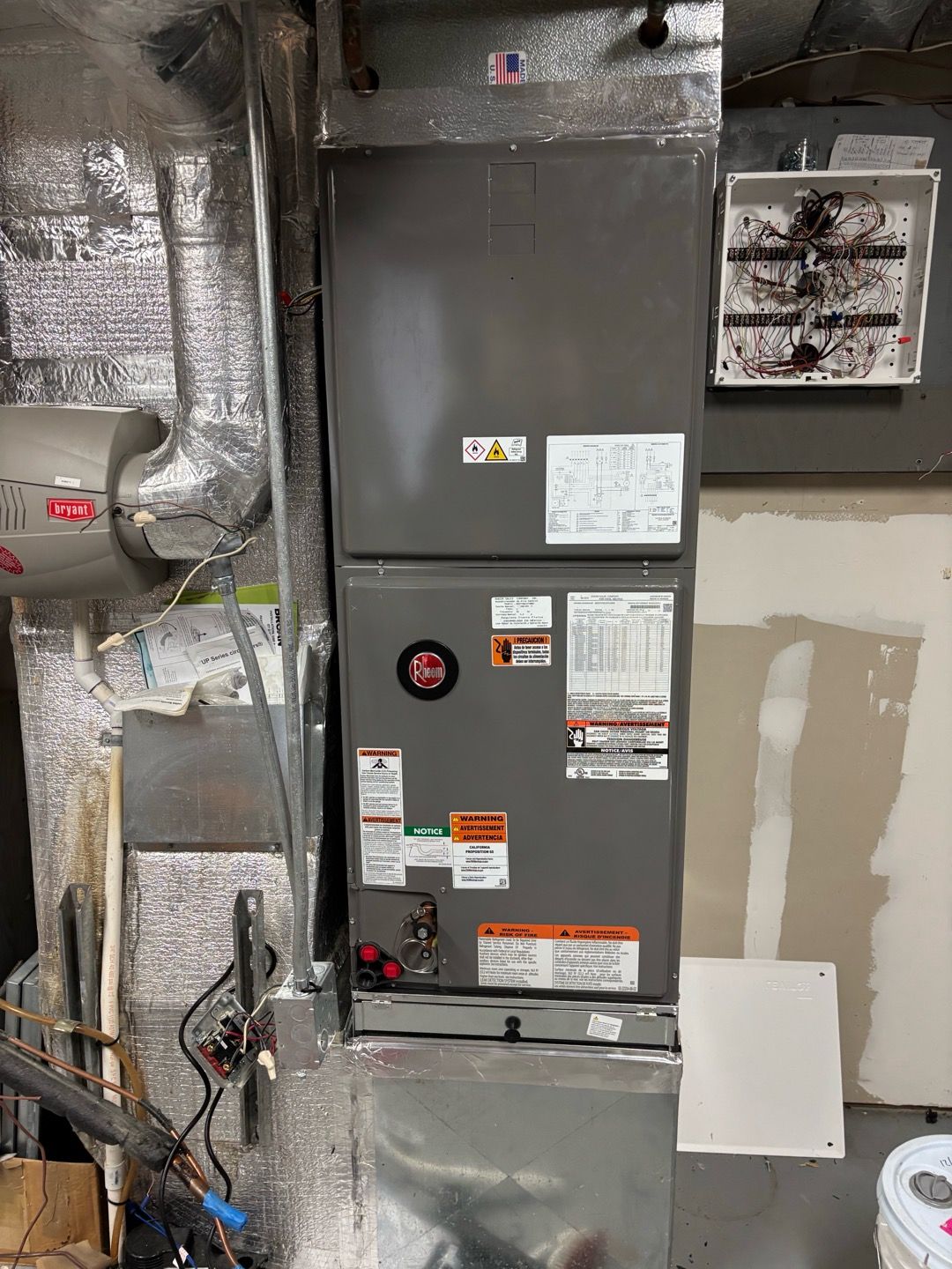HVAC furnace and ductwork in a utility closet with foil insulation and a white wall panel