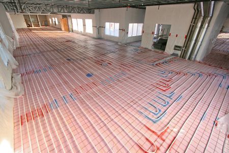 Indoor construction site with red underfloor heating pipes laid across a concrete floor