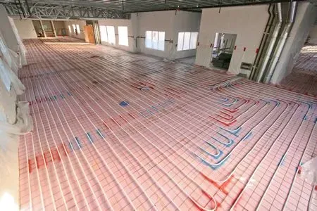 Construction site floor with pink underfloor heating pipes laid over insulation in a large unfinished room