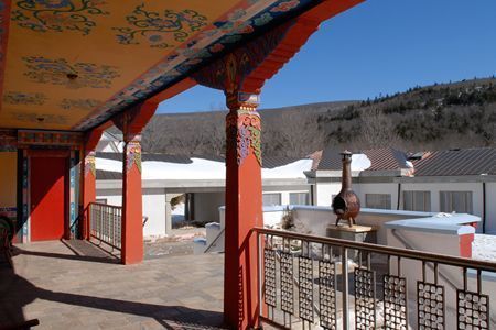 Covered terrace with red columns overlooking snowy rooftops and hills under a clear blue sky