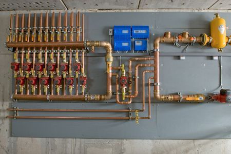 Copper manifold plumbing system with blue controls and yellow tank mounted on a wall