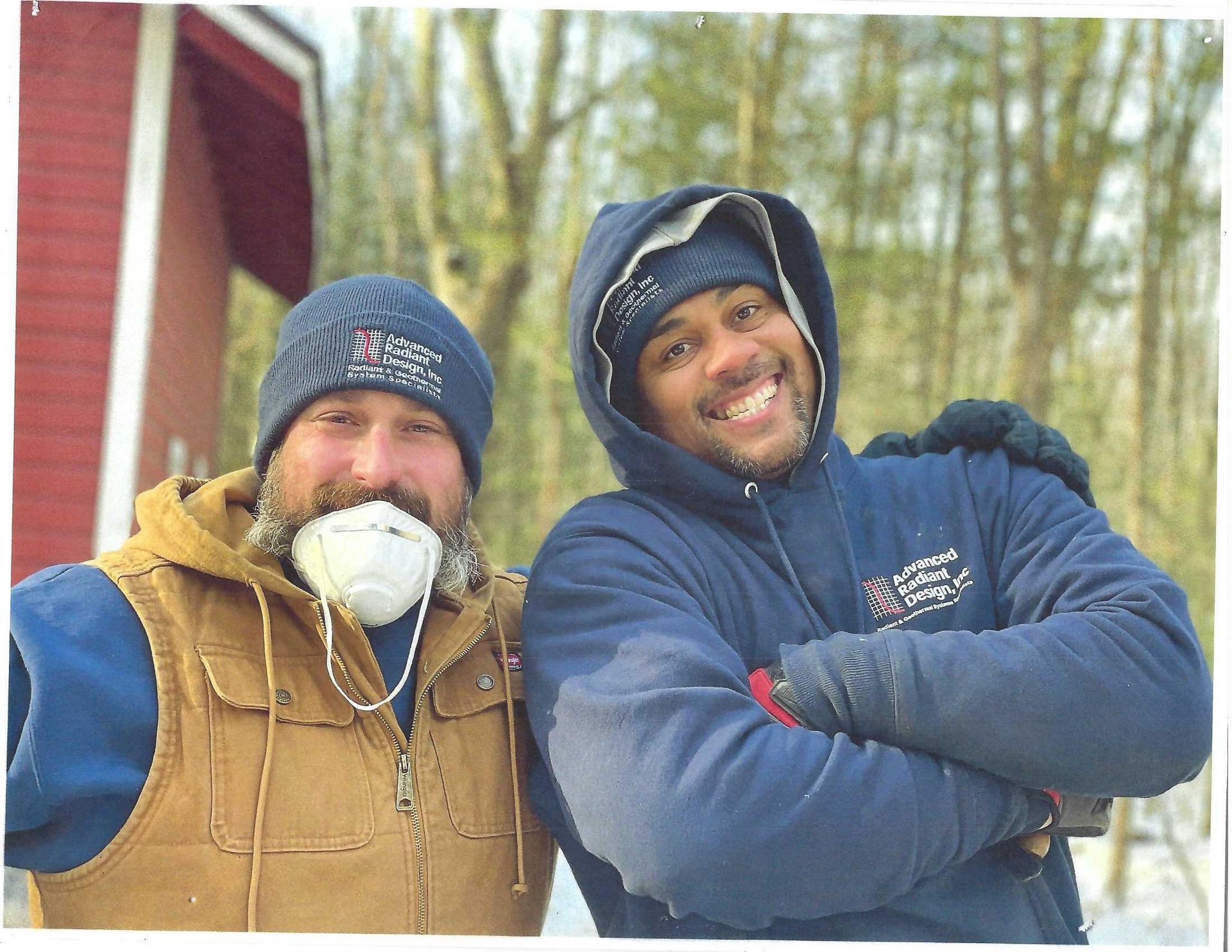 Two bundled-up people smiling outdoors in winter, one wearing a face mask and the other a blue hooded jacket